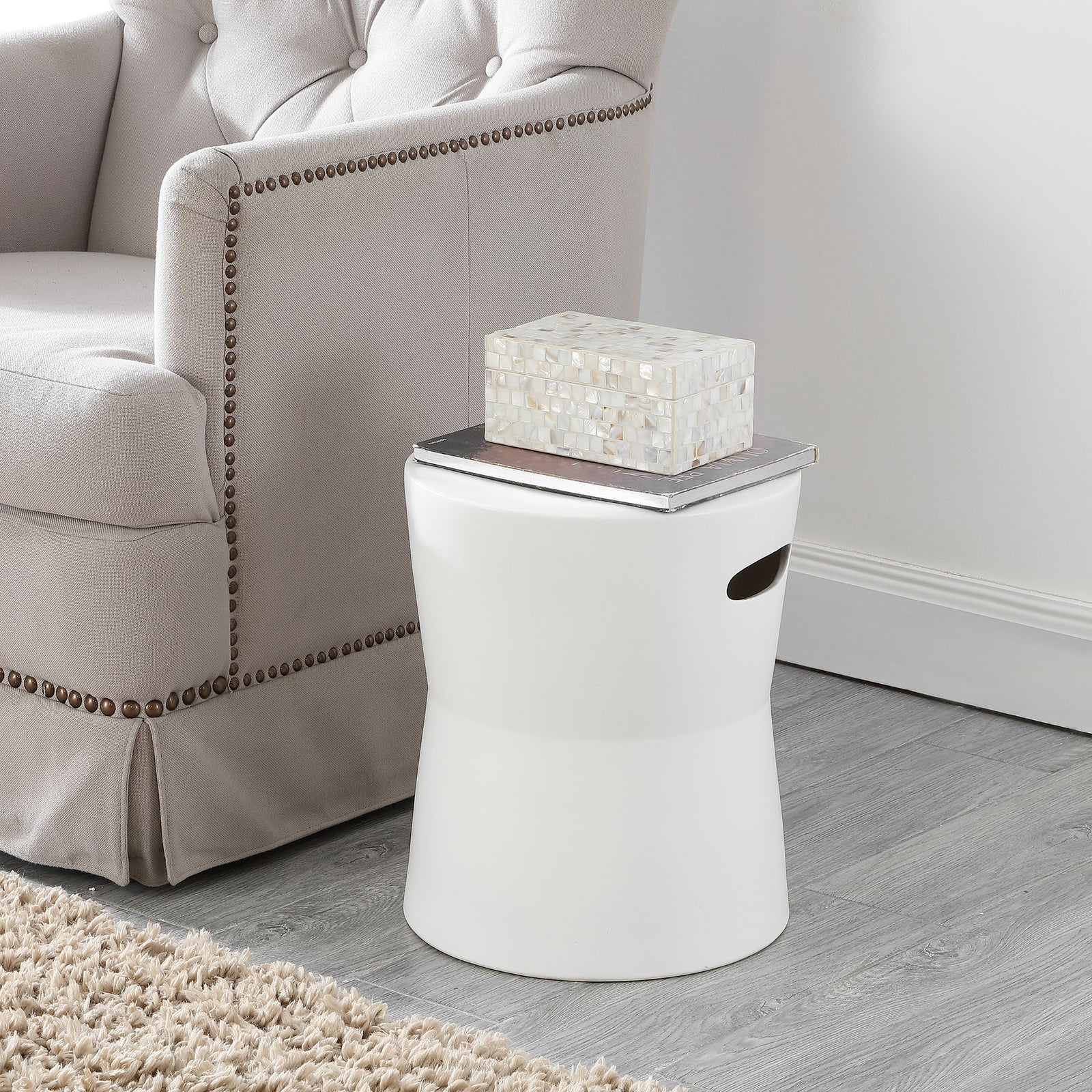 Matte white ceramic stool serves as a compact side table beside an upholstered chair || ACS4599A || front_angle_room