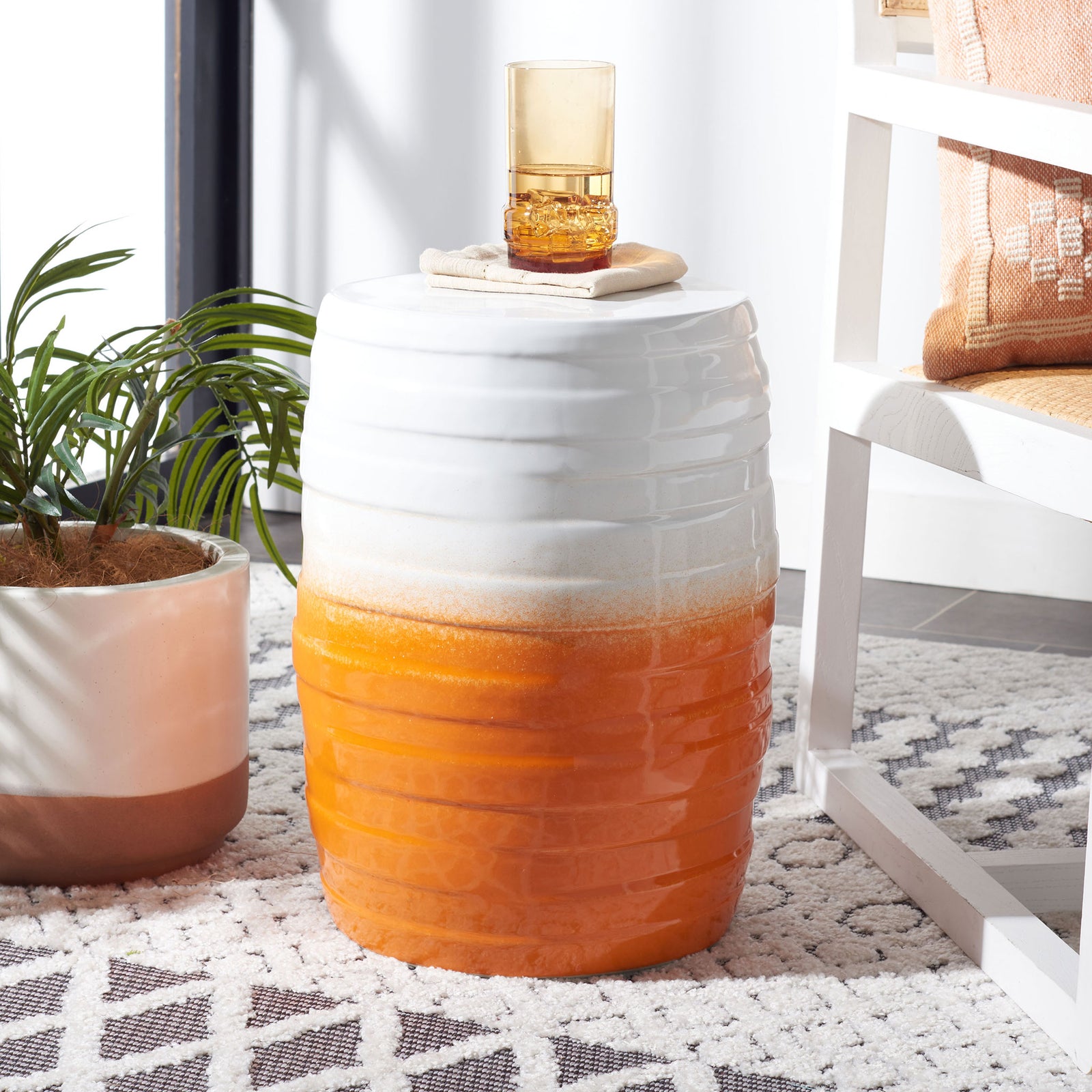 A bright orange-and-white ceramic garden stool doubles as a side table beside a chair. || ACS5201C || front_angle_room