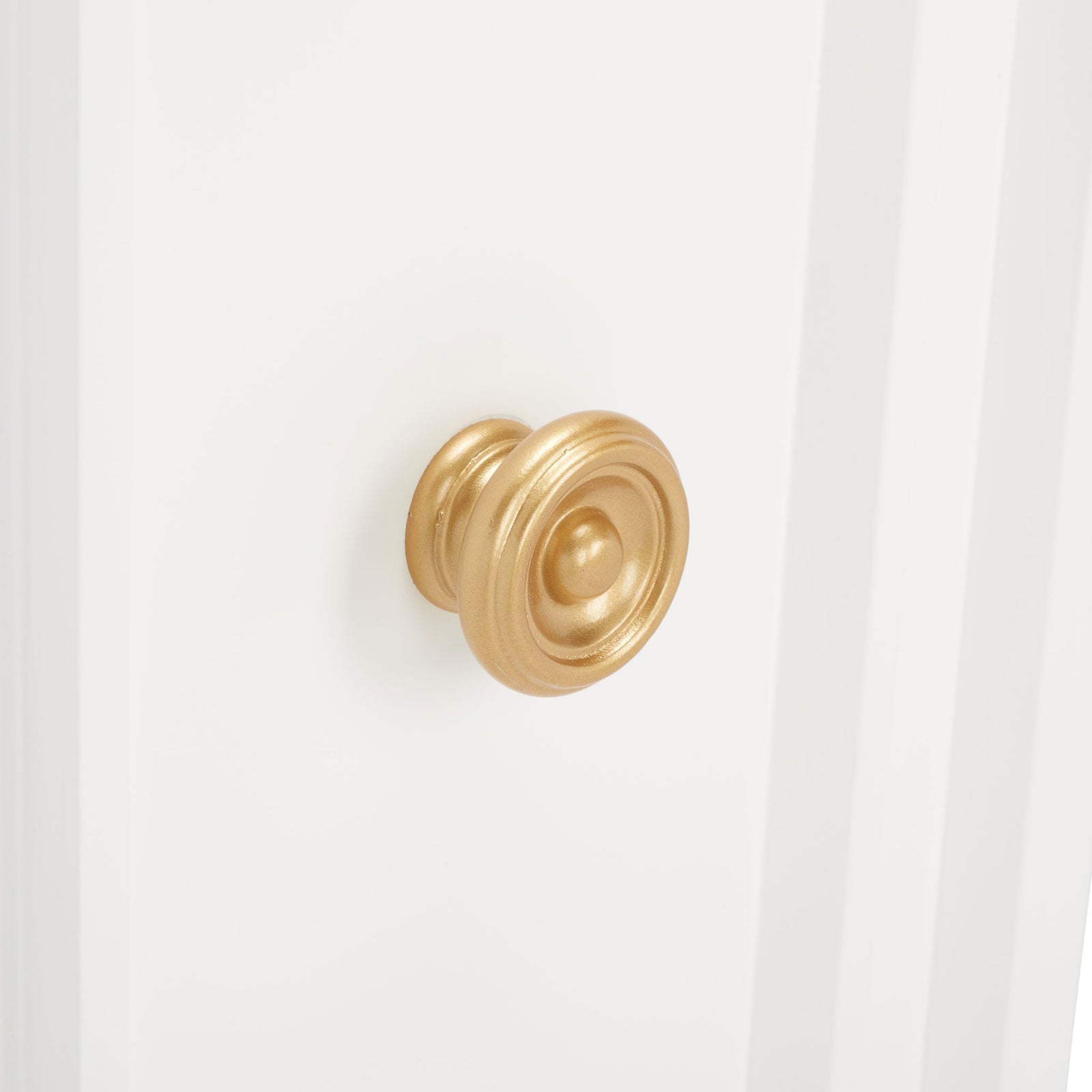 An ornate gold-tone knob adds a warm metallic accent to the crisp white cabinet door. || CHS5003A || handle_studio
