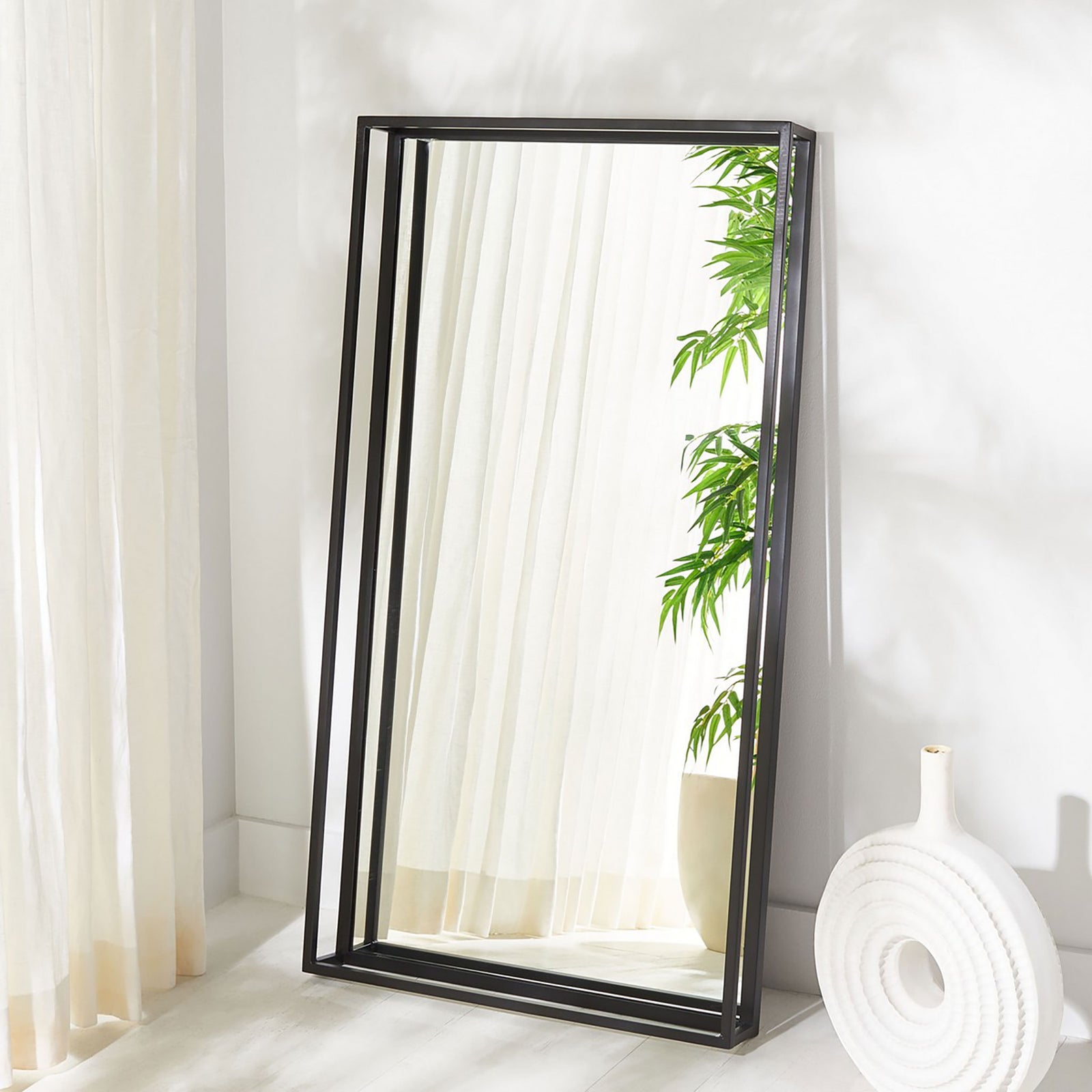A tall black shadow box mirror adds depth and reflection to a bright room. || CMI1001A || front_angle_room