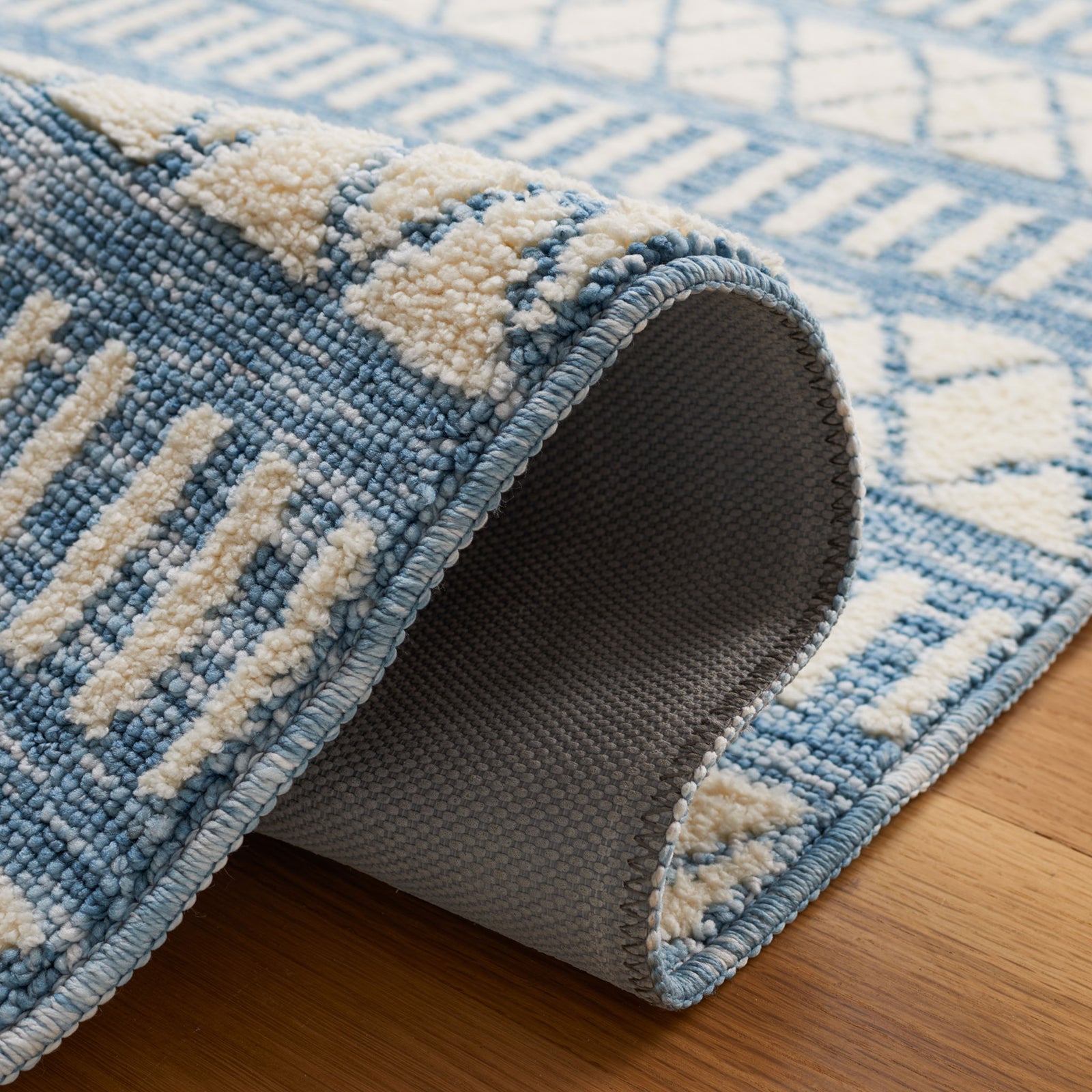 Folded edge reveals the latex backing and dense texture of the ivory and blue rug || ECR114A-5 || backing_room