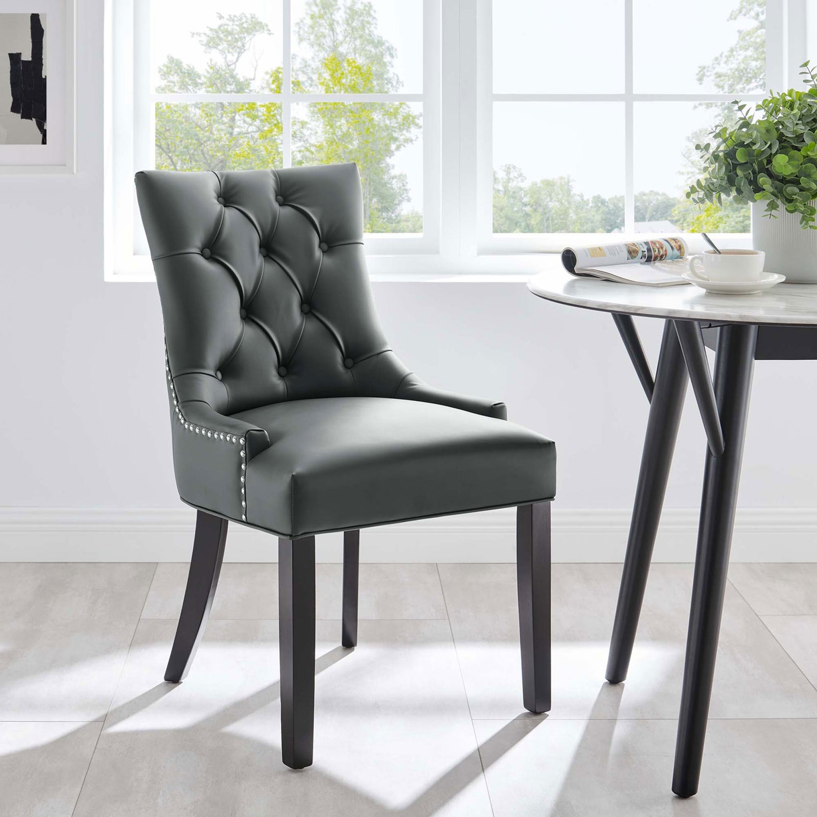 Gray tufted vegan leather dining chair styled beside a modern round dining table in a bright airy room || EEI-2222-GRY || front_angle_room