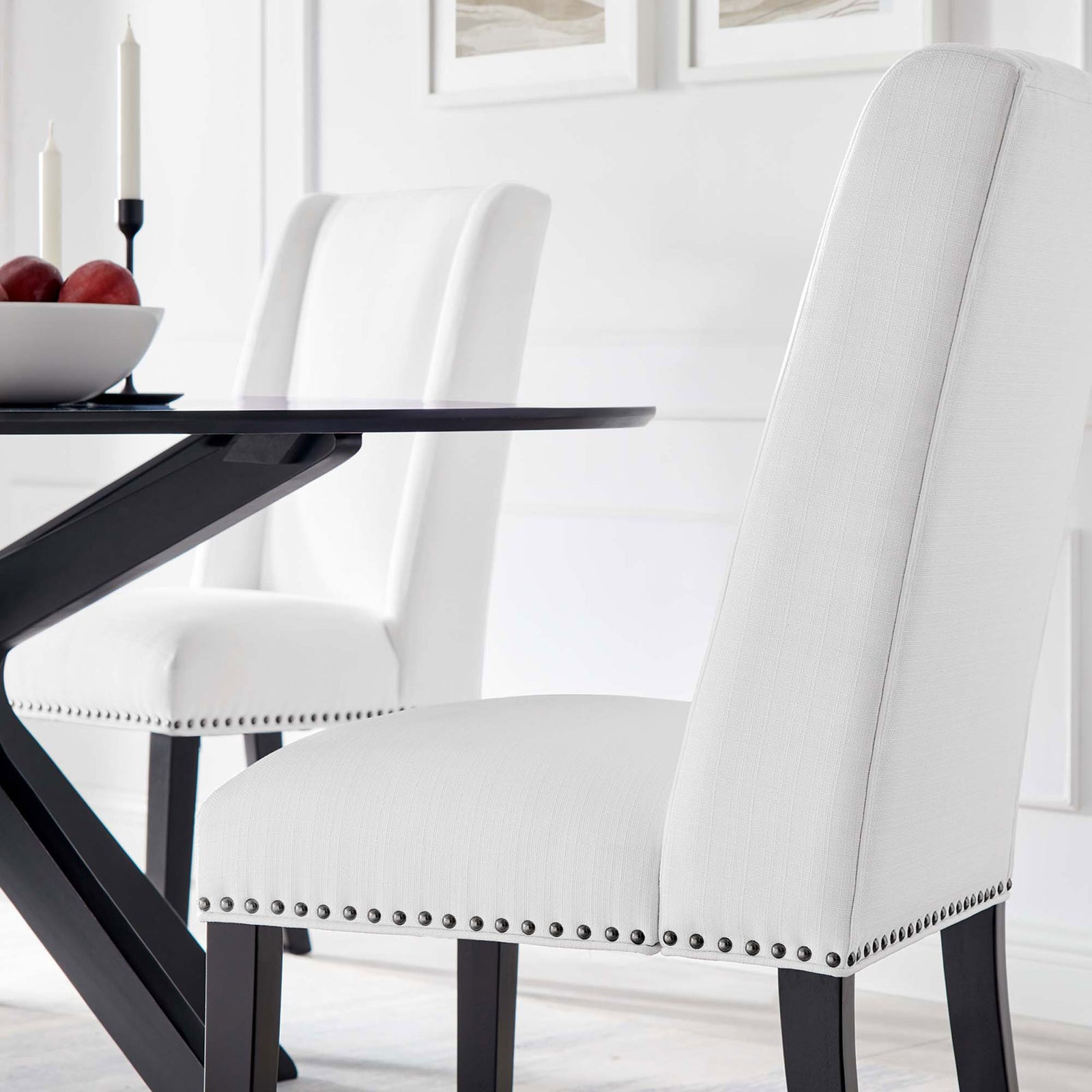 Two white dining chairs with nailhead trim styled at a modern black dining table in bright room || EEI-2233-WHI || front_angle_room