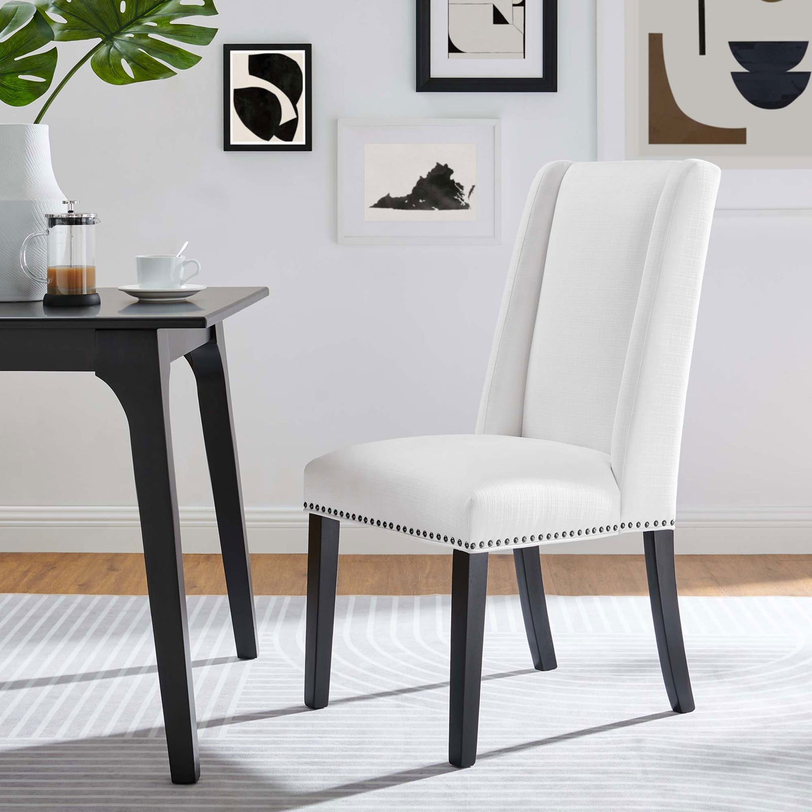 White upholstered dining chair with nailhead accents in a contemporary room with wall art || EEI-2233-WHI || front_angle_room