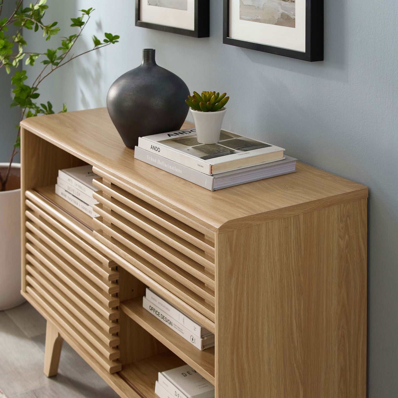 Oak display stand styled in a modern living room with books, decor accents, and indoor plant || EEI-2542-OAK || front_angle_room