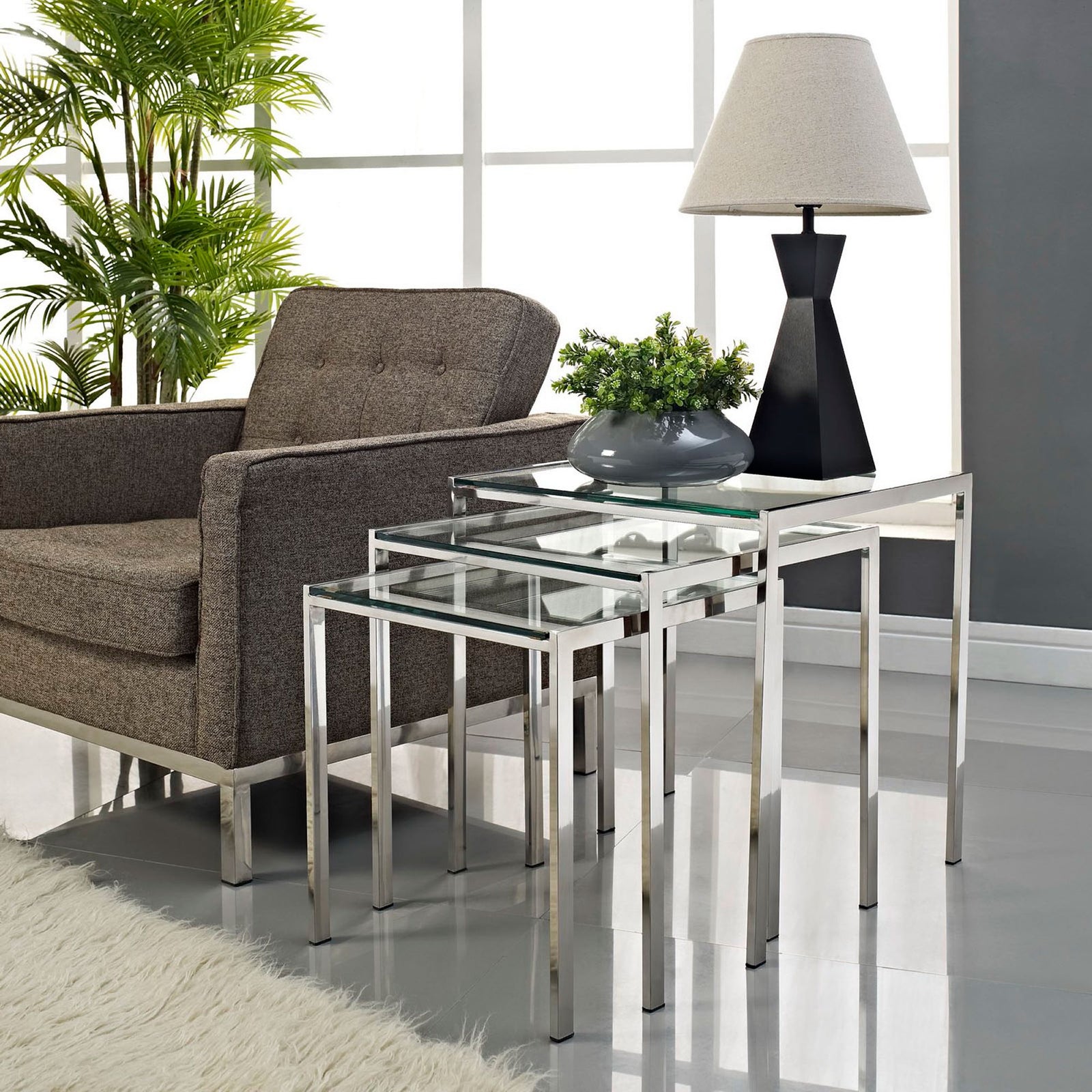 Silver glass nesting tables styled beside a sofa with decor accents for a bright contemporary living room. || EEI-257 || front_angle_room