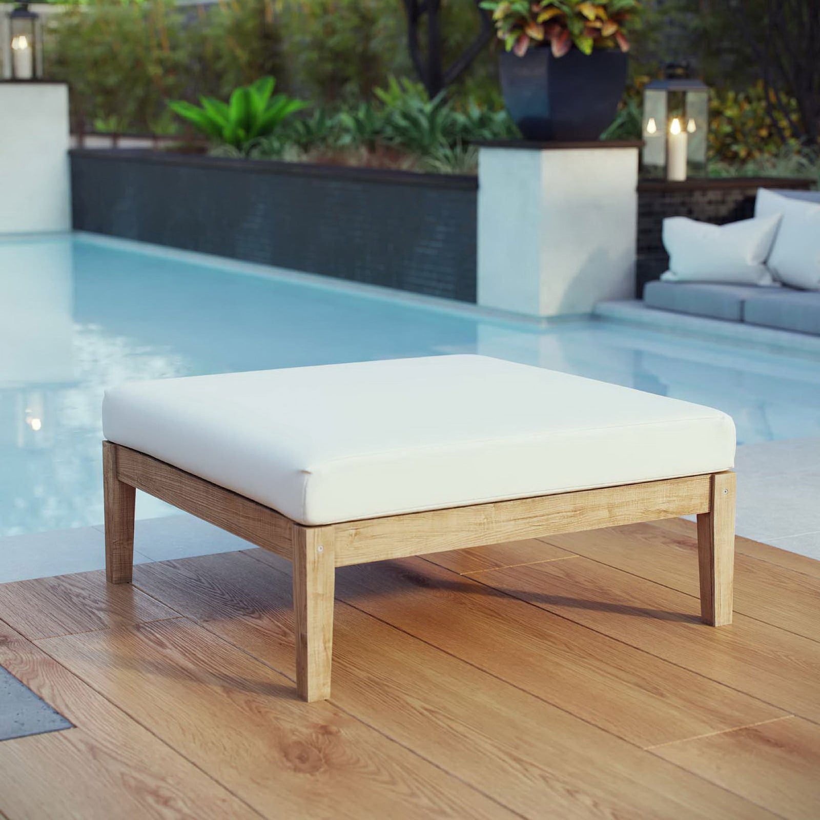 Teak outdoor ottoman with white cushion styled beside a pool for resort-inspired lounging || EEI-2698-NAT-WHI || front_angle_room