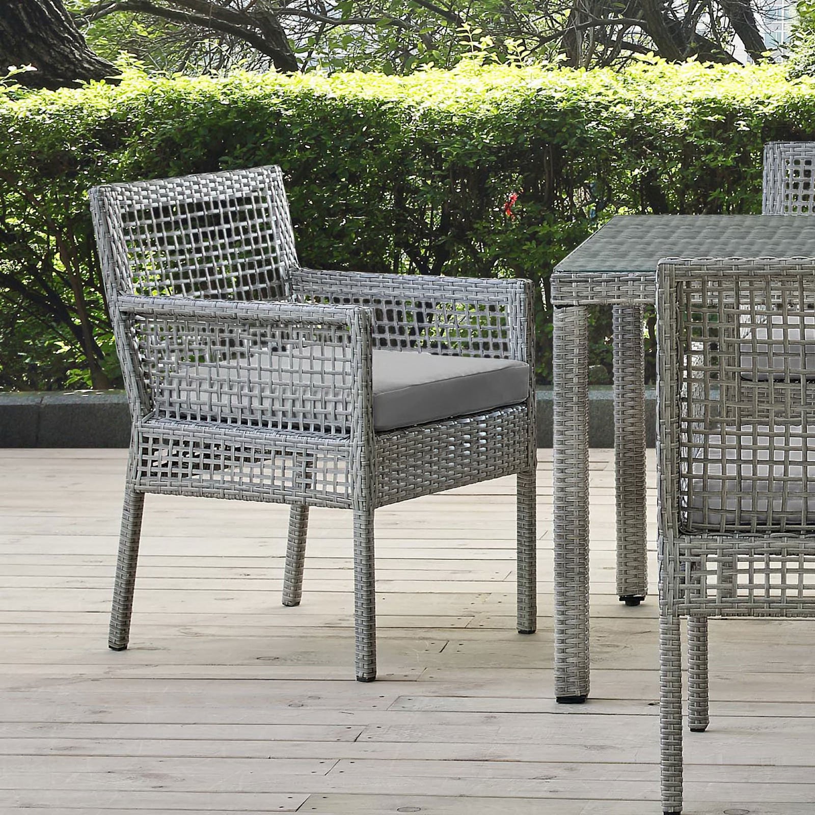 Aura gray wicker outdoor dining armchair with gray cushion styled on a patio beside a matching dining table || EEI-2920-GRY-GRY || front_angle_room