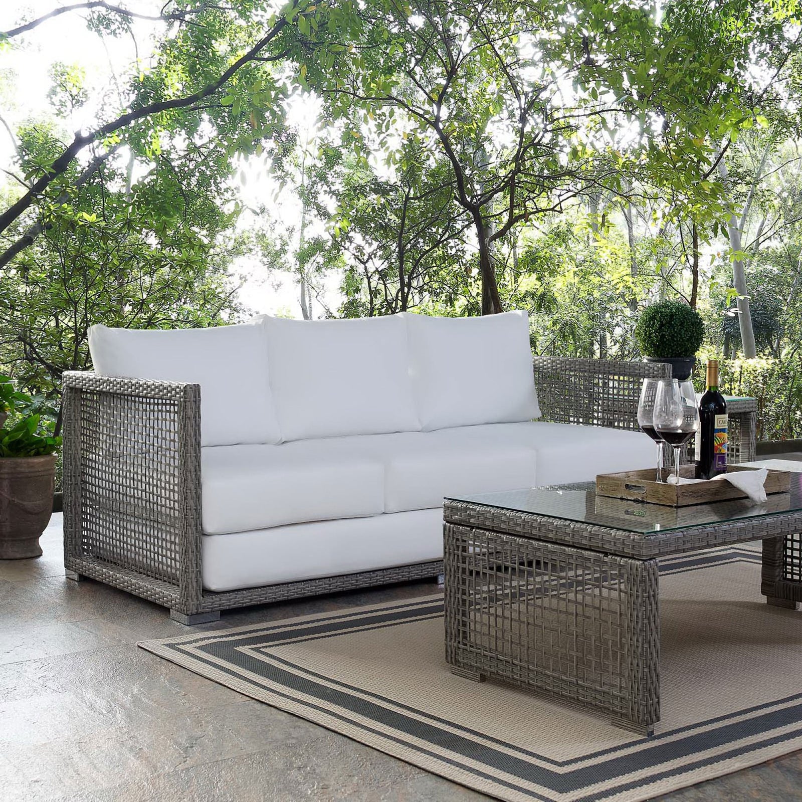 Gray wicker sofa with bright white cushions styled on a patio with coordinating woven coffee table || EEI-2923-GRY-WHI || front_angle_room