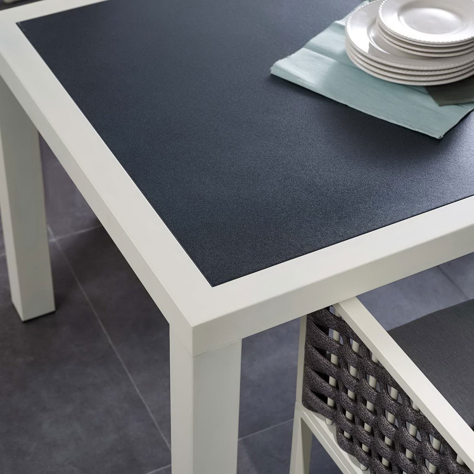 Dining table styled with outdoor dishware and woven chairs, showing the dark top against the white frame || EEI-3052-WHI-GRY || detail_room