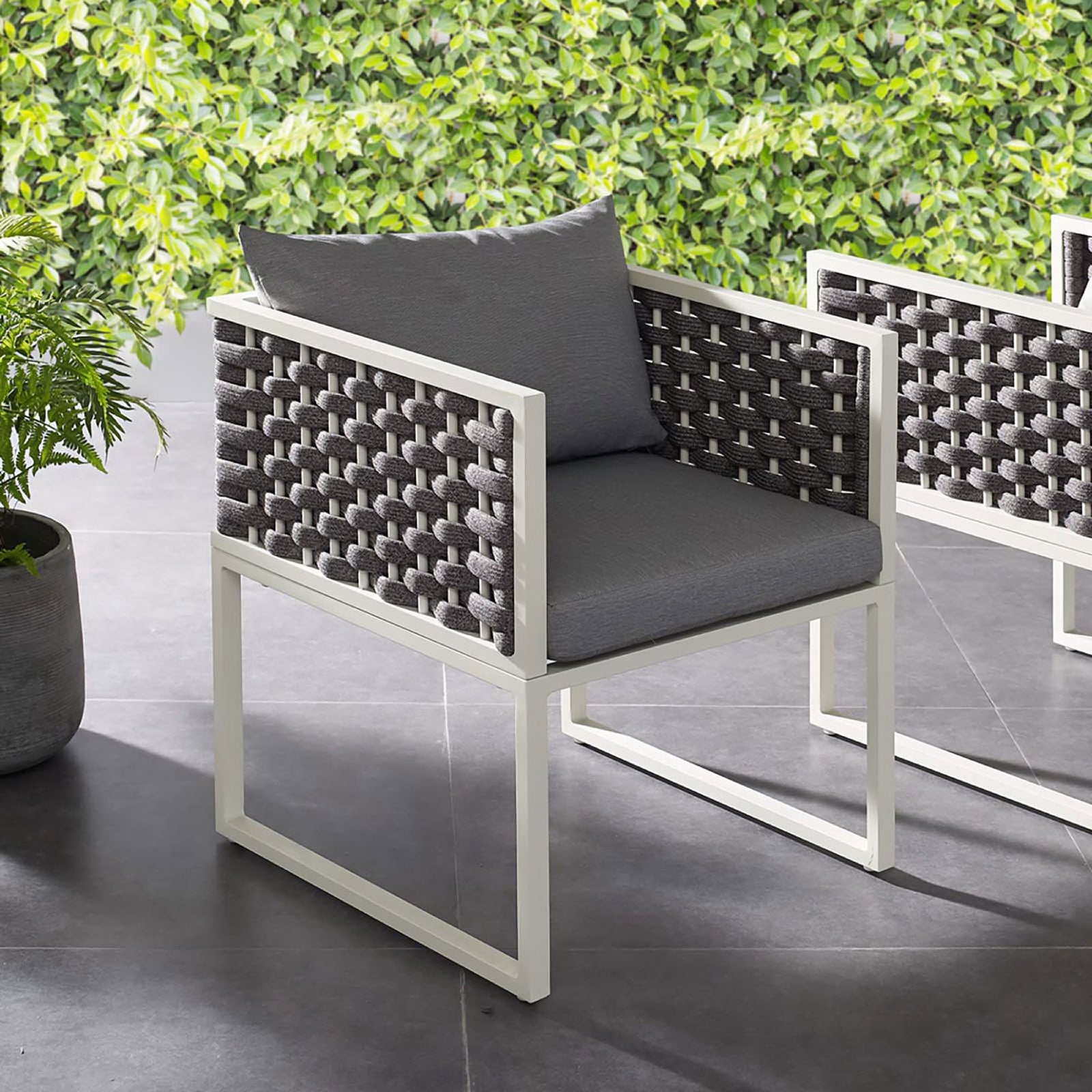 Gray cushioned outdoor dining armchair with white frame styled on a modern patio beside greenery || EEI-3053-WHI-GRY || front_angle_room