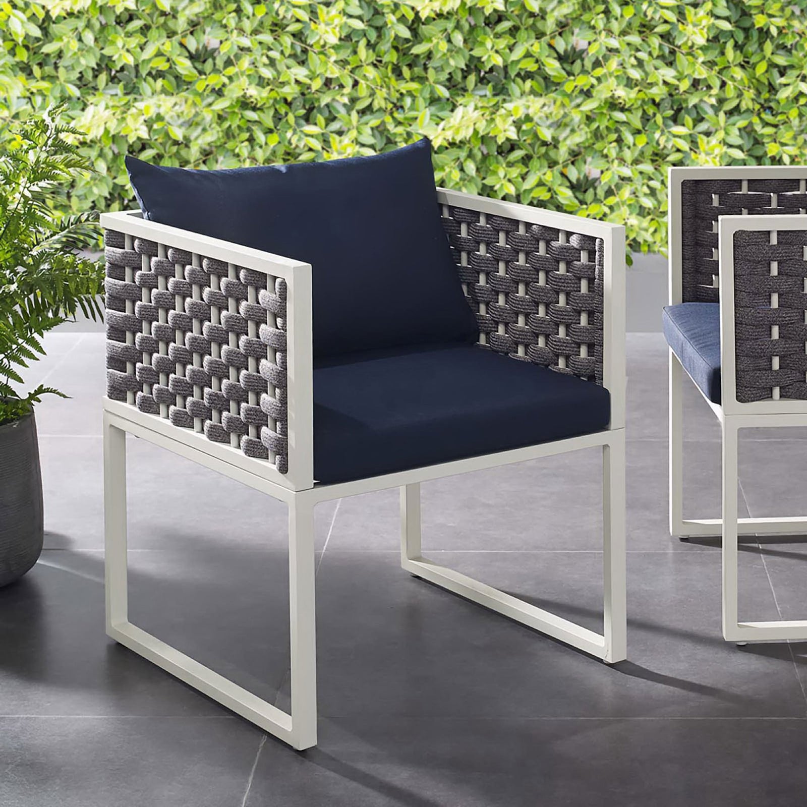 Navy cushioned outdoor dining armchair with white frame styled on a modern patio beside greenery || EEI-3053-WHI-NAV || front_angle_room