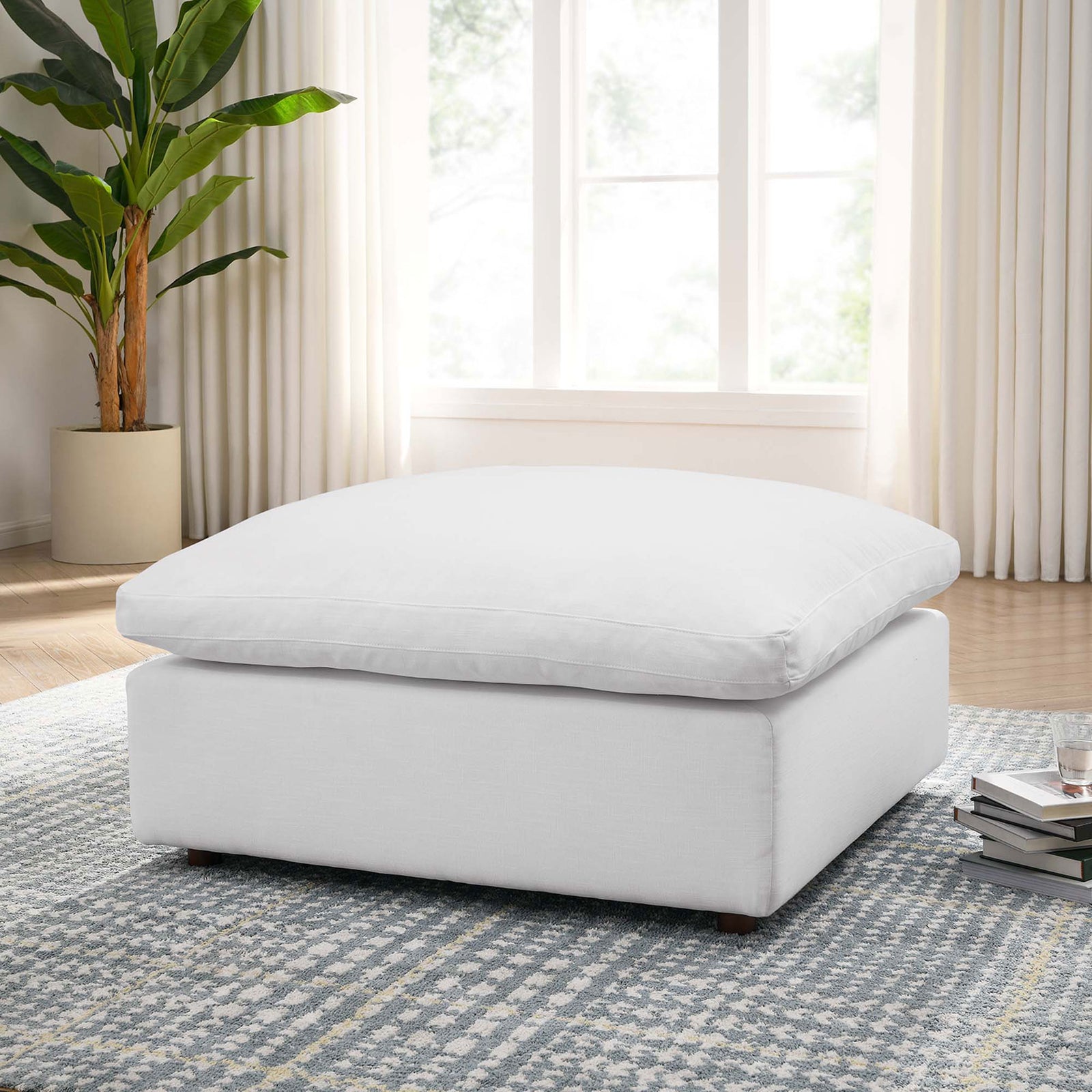 Commix pure white ottoman styled in a bright living room on a patterned rug beside books and a glass of water || EEI-3318-PUW || front_angle_room