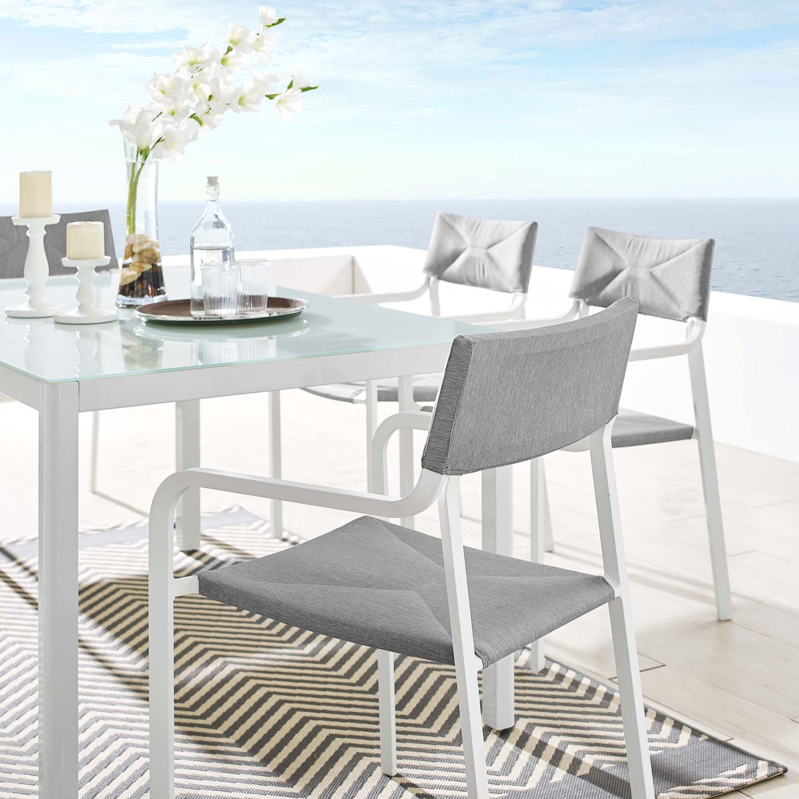Gray upholstered Raleigh patio chair beside a modern outdoor dining table on a terrace || EEI-3573-WHI-GRY || front_angle_room