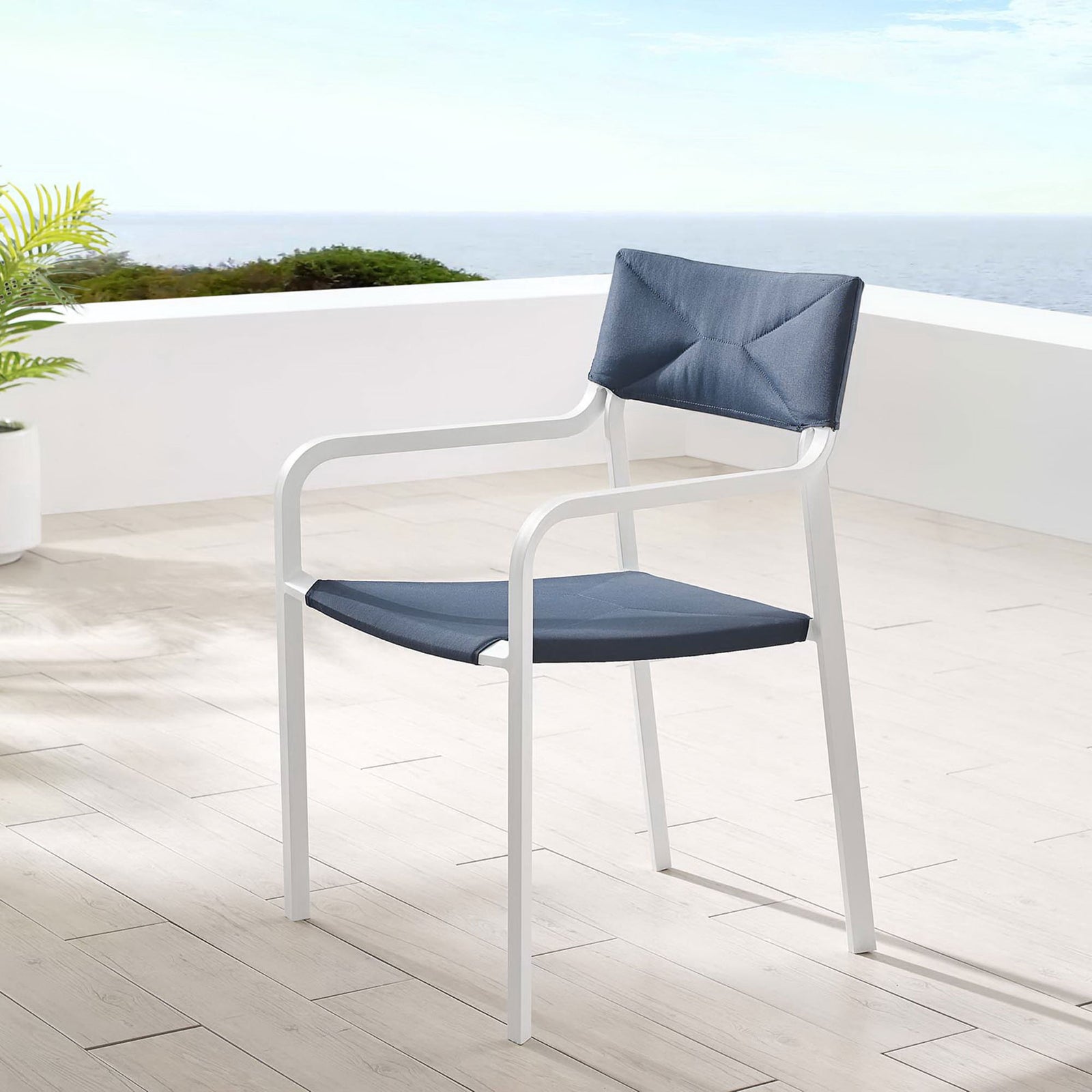 Navy upholstered Raleigh patio chair on a sunny terrace overlooking lush greenery || EEI-3573-WHI-NAV || front_angle_room
