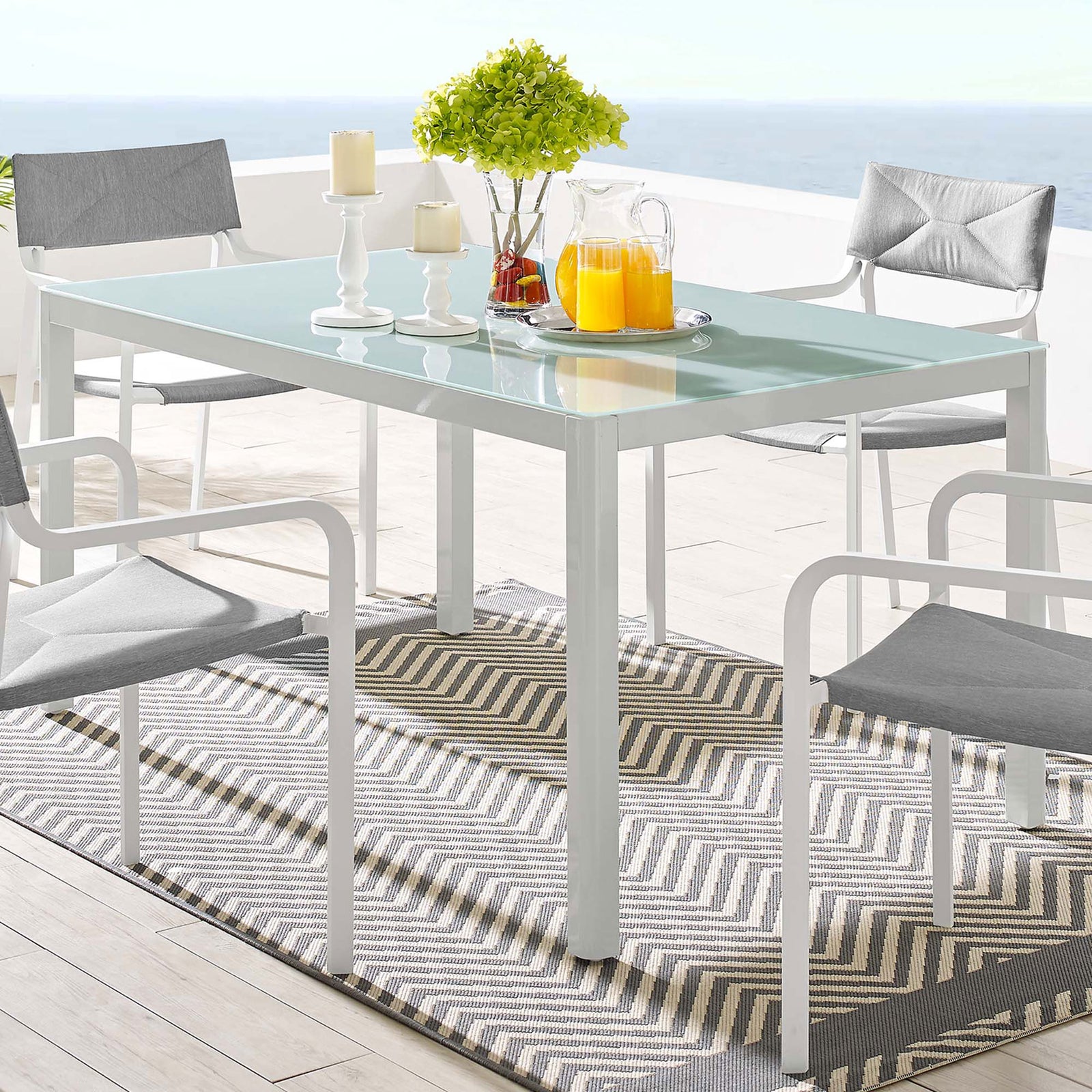 White outdoor dining table on a balcony with bright decor and ocean backdrop for relaxed dining || EEI-3576-WHI || front_angle_room