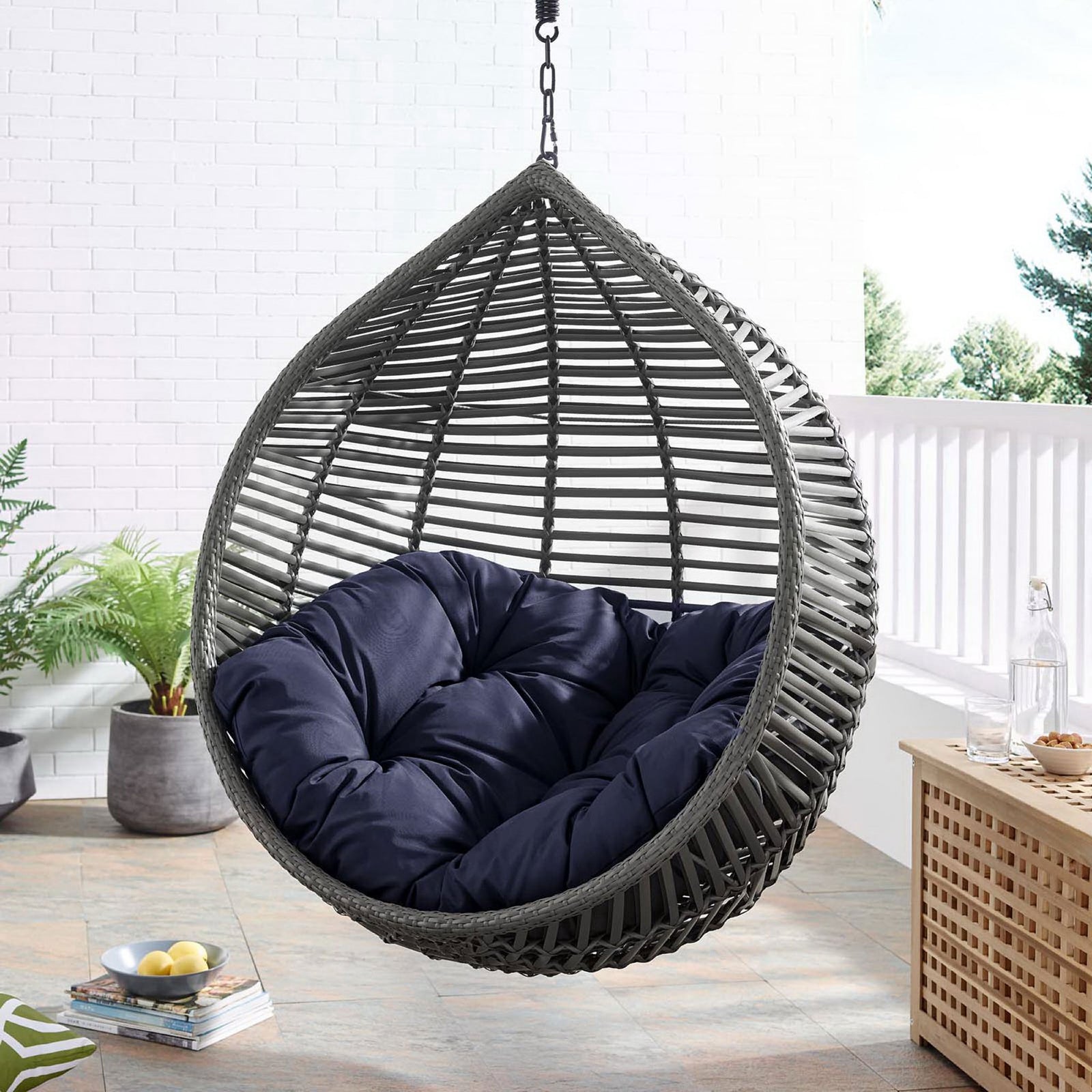 Hanging teardrop chair with navy cushion adding bold color and comfort to a bright outdoor patio. || EEI-3614-GRY-NAV || front_angle_room