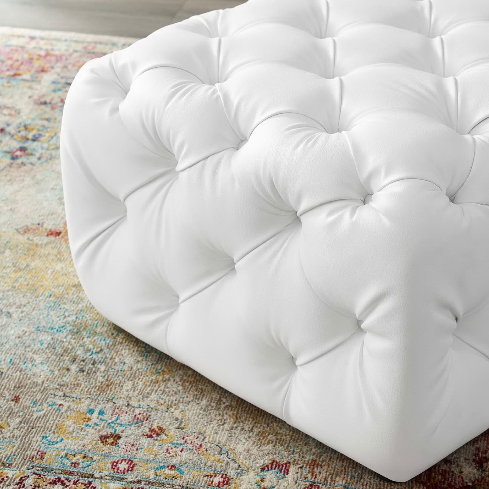 White tufted faux leather ottoman corner resting on a colorful patterned rug || EEI-3775-WHI || detail_room