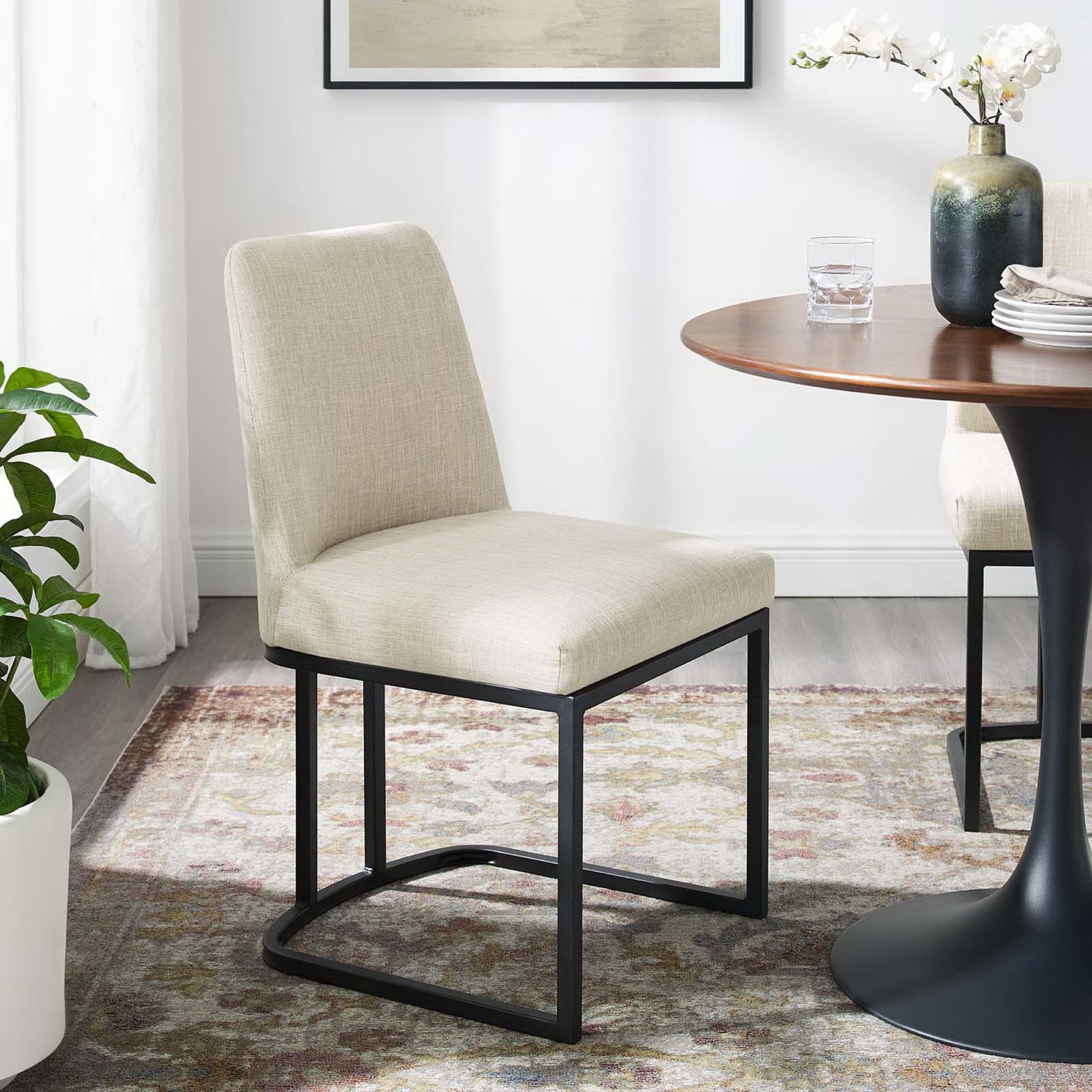 Beige sled base dining chair styled beside a round wood dining table on a patterned rug || EEI-3811-BLK-BEI || front_angle_room