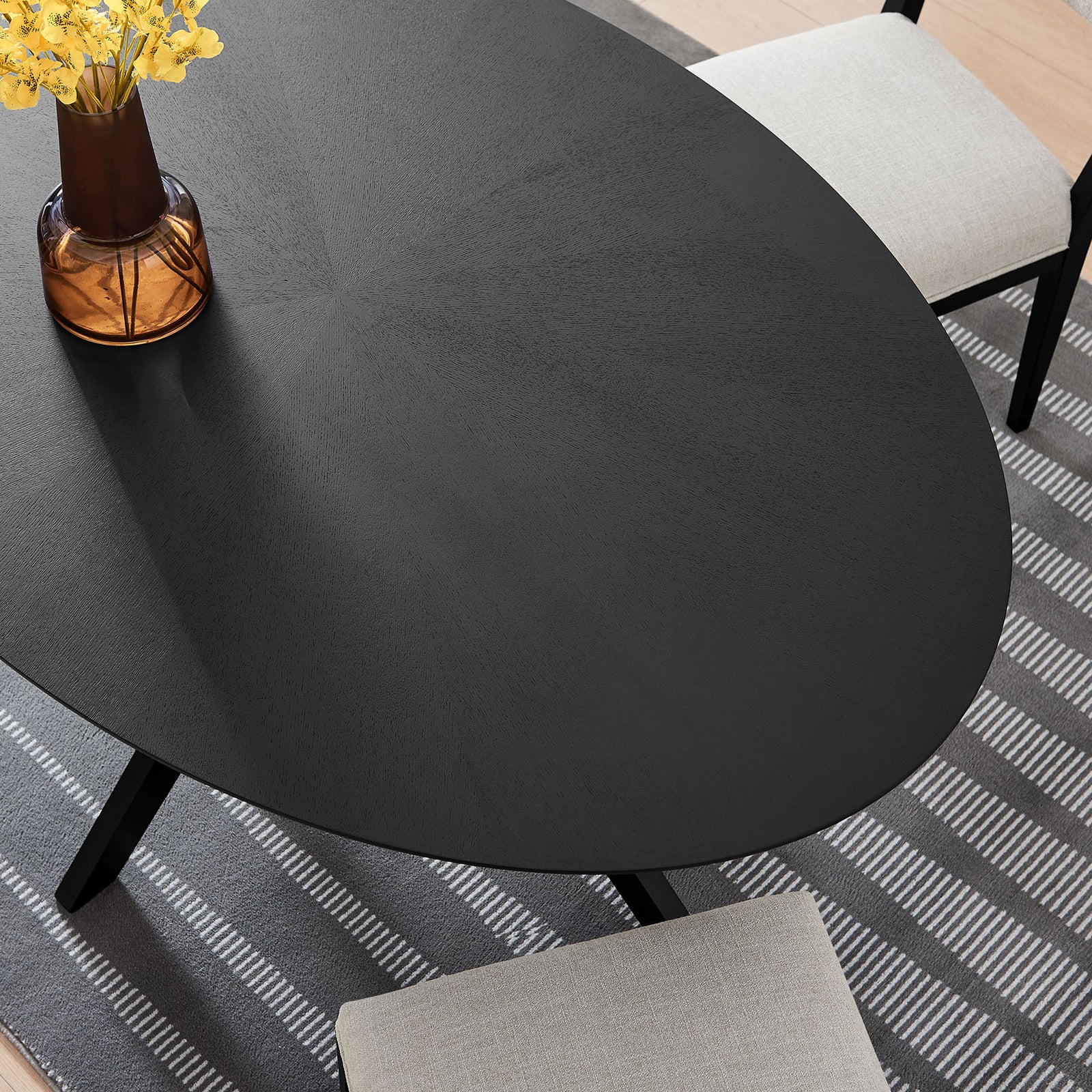 Detail of black oval tabletop arranged with vase, flowers, and place settings over a patterned rug || EEI-3848-BLK || detail_room