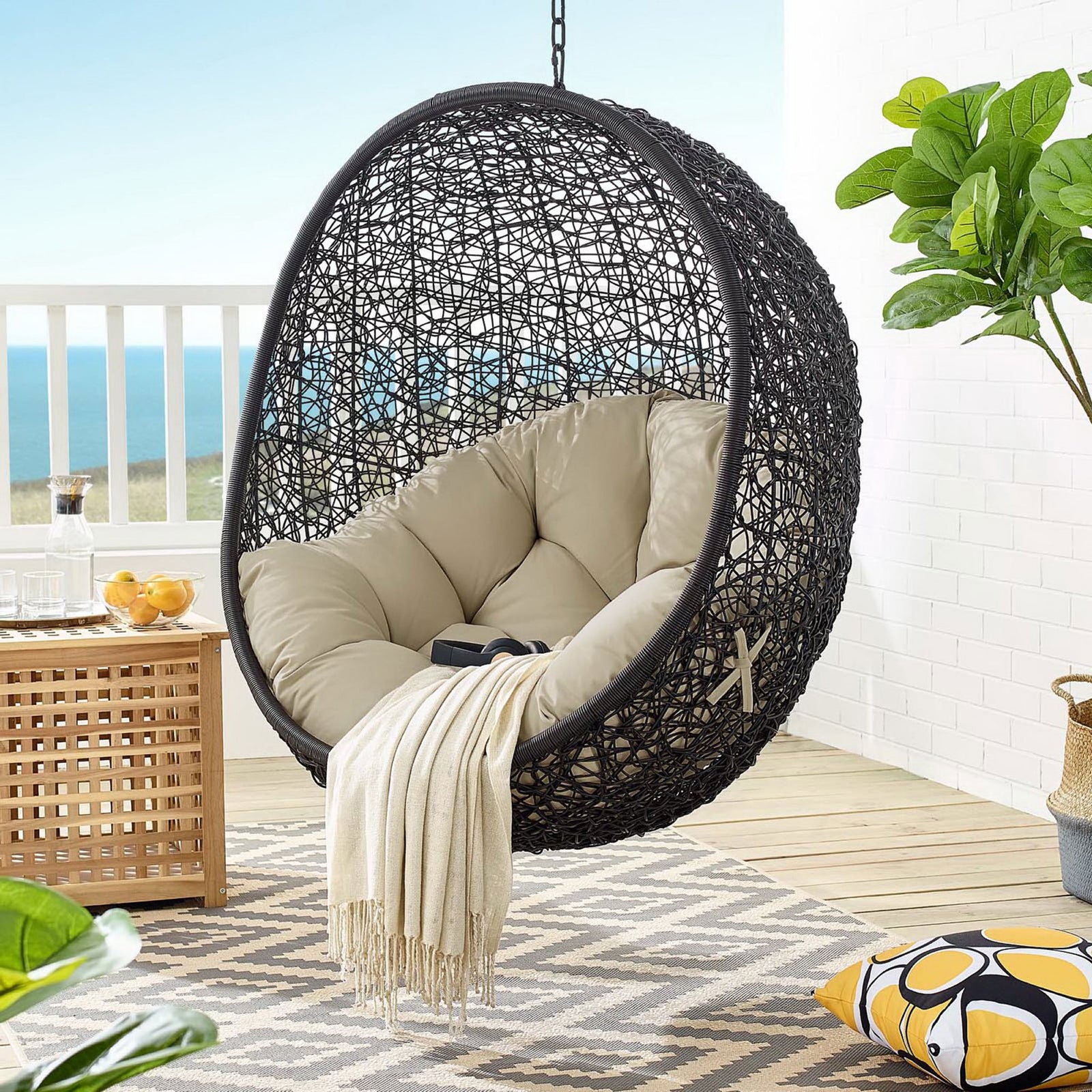 Suspended beige Sunbrella egg chair creating a cozy retreat on a breezy oceanfront balcony || EEI-3943-BLK-BEI || front_angle_partial_room