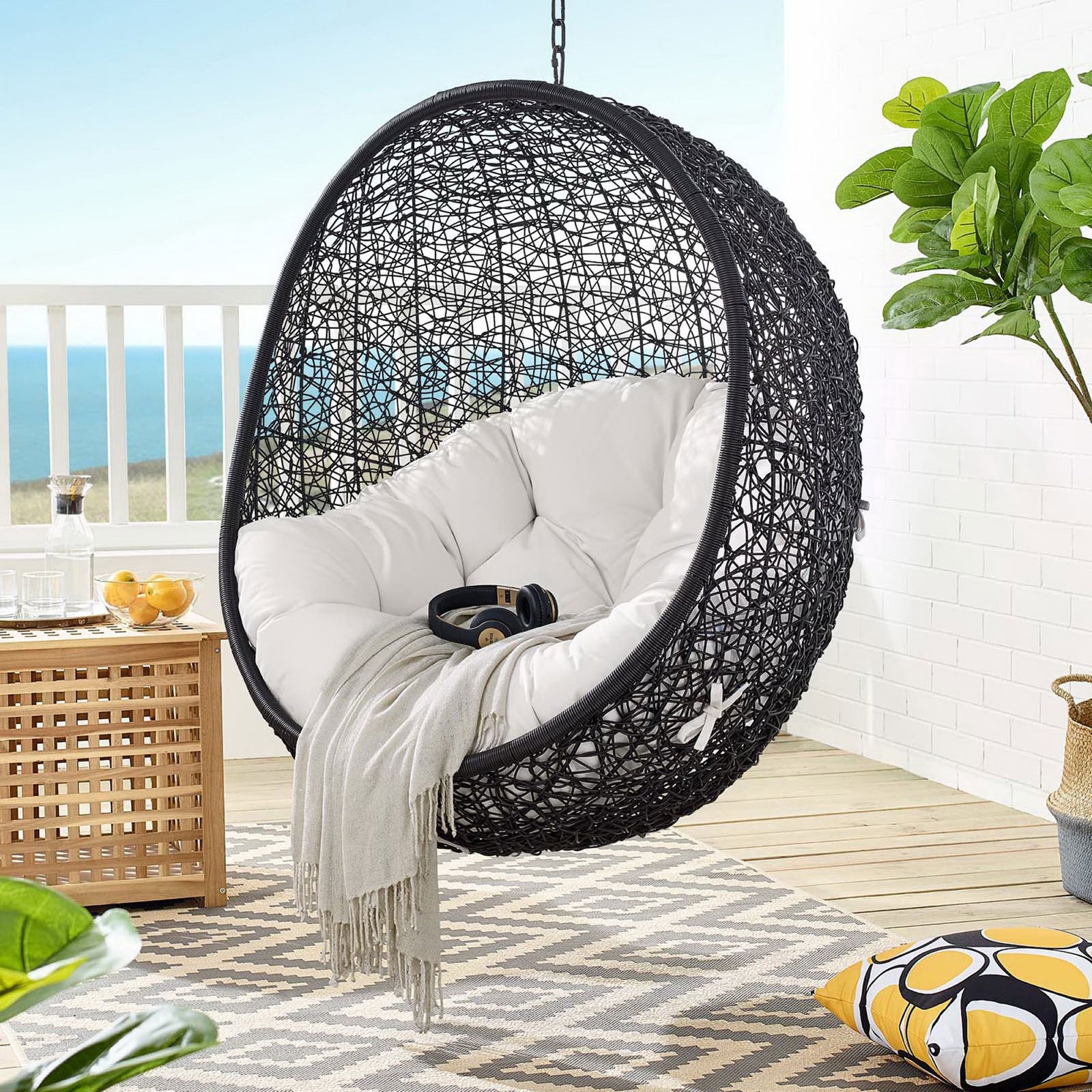 Suspended white Sunbrella swing chair creating a serene outdoor retreat with ocean views || EEI-3943-BLK-WHI || front_angle_partial_room