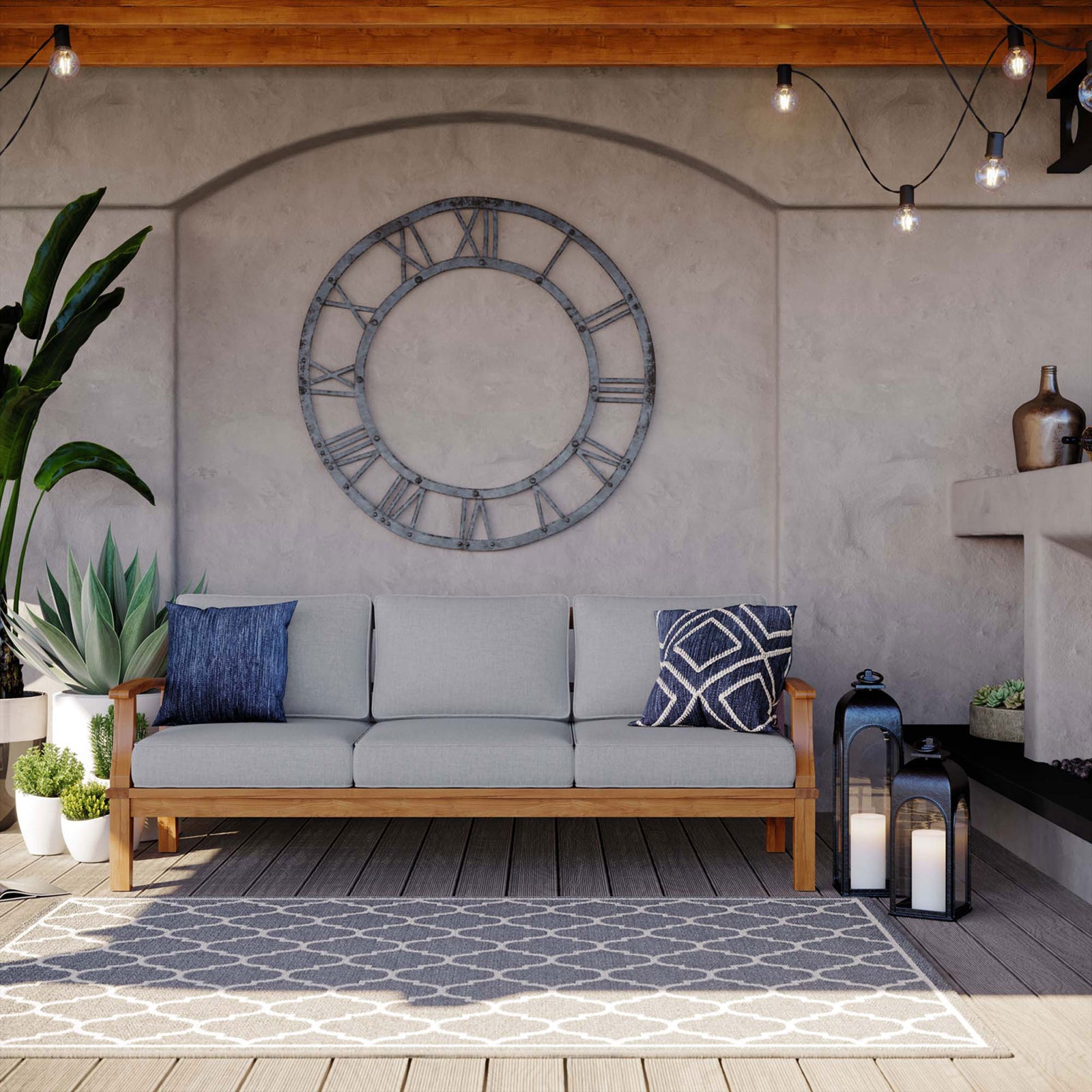 Gray cushioned teak sofa styled on a cozy patio with lanterns, rug, and wall clock decor || EEI-4176-NAT-GRY || front_angle_room
