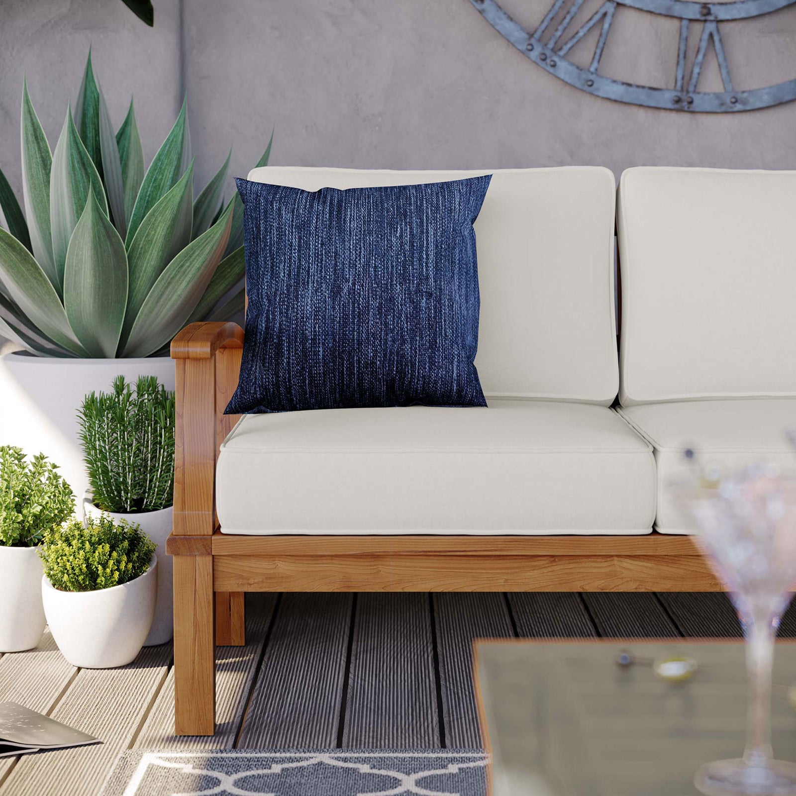 Teak patio sofa corner with white cushions, blue throw pillow, and lush potted plants || EEI-4176-NAT-WHI || detail_room