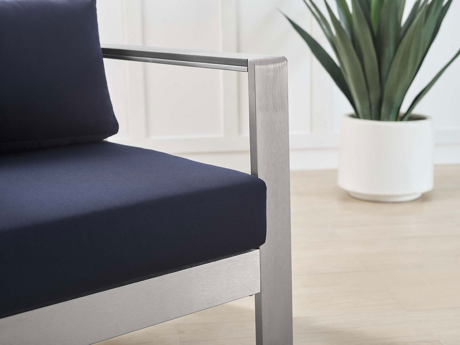 Smooth armrest and tailored navy cushion sit over light decking for a refined patio look || EEI-4225-SLV-NAV || detail_room