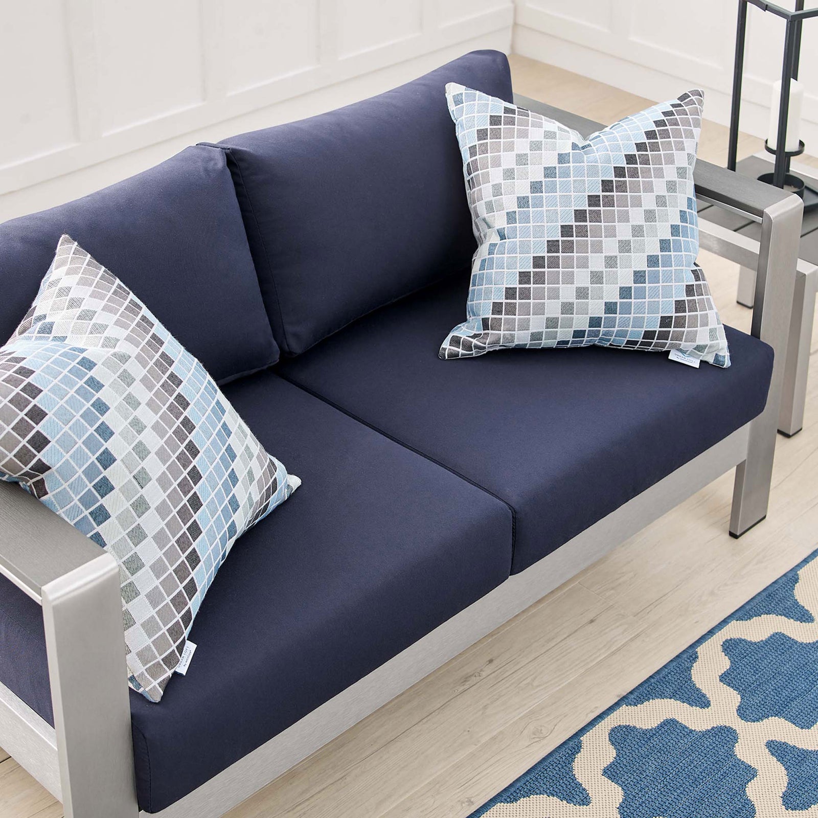 Overhead detail of navy loveseat cushions with patterned accent pillows and light wood flooring || EEI-4226-SLV-NAV || detail_room