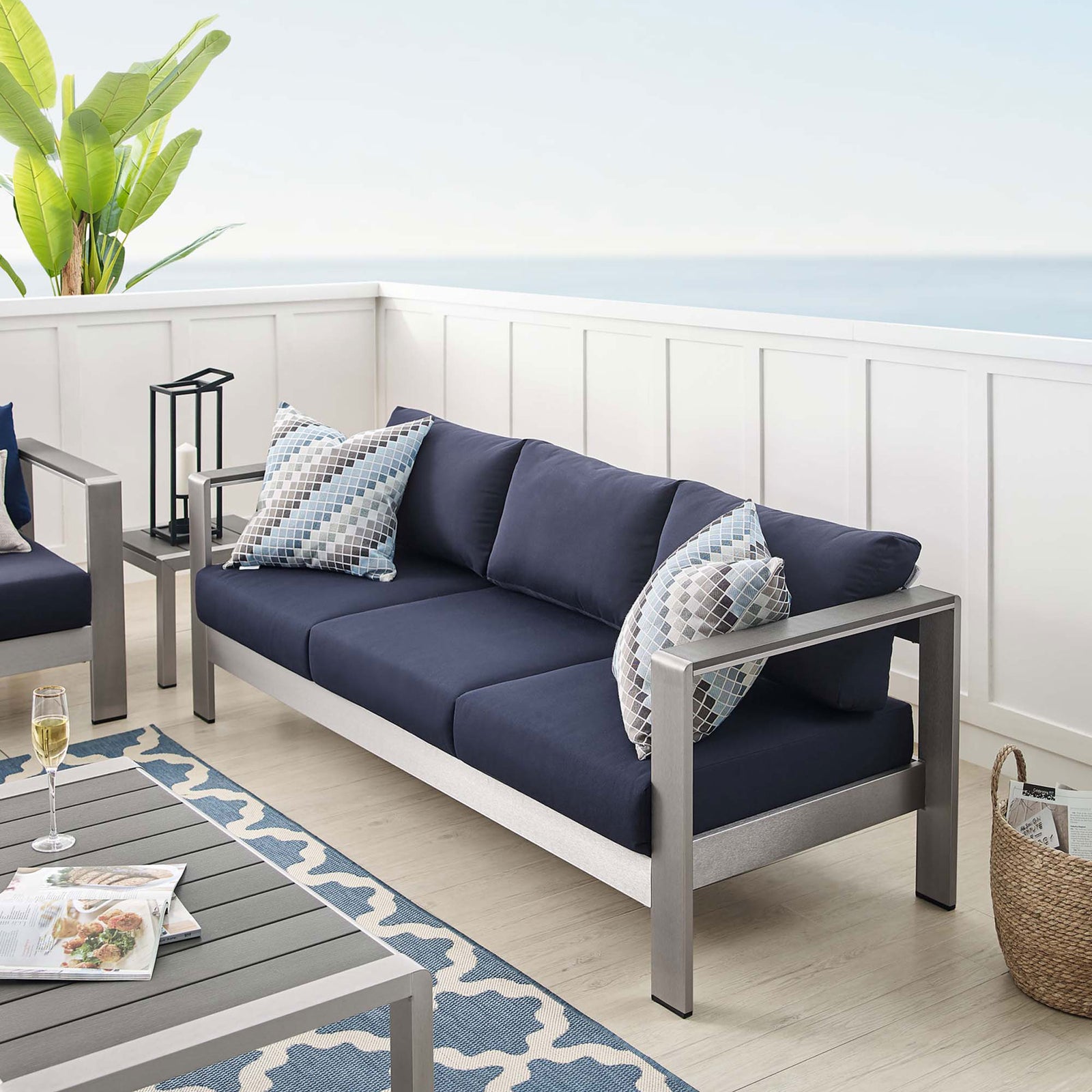 Navy cushioned Shore sofa completes a coastal-inspired patio with light flooring and blue rug accents || EEI-4228-SLV-NAV || front_angle_room