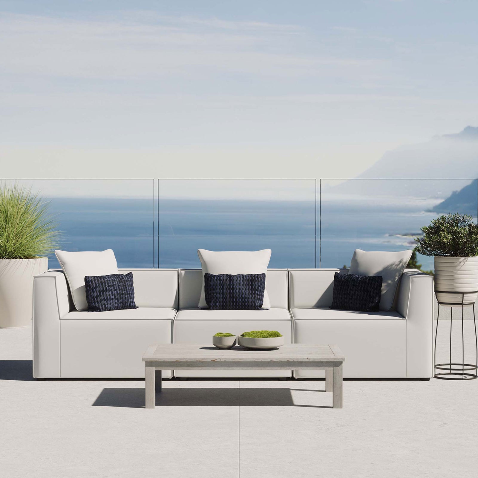 White outdoor sectional sofa with accent pillows styled on a sunlit patio by the ocean. || EEI-4379-WHI || front_room
