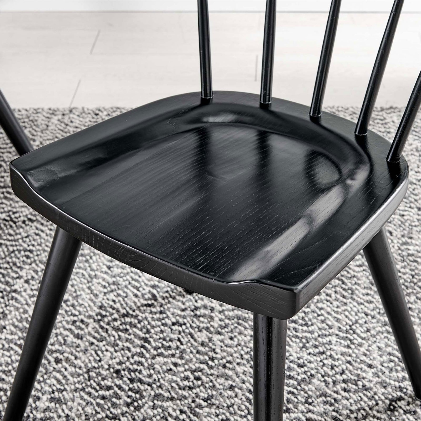 Black wood seat over a textured neutral rug, showing the chair's molded contours and soft sheen. || EEI-4650-BLK || detail_room
