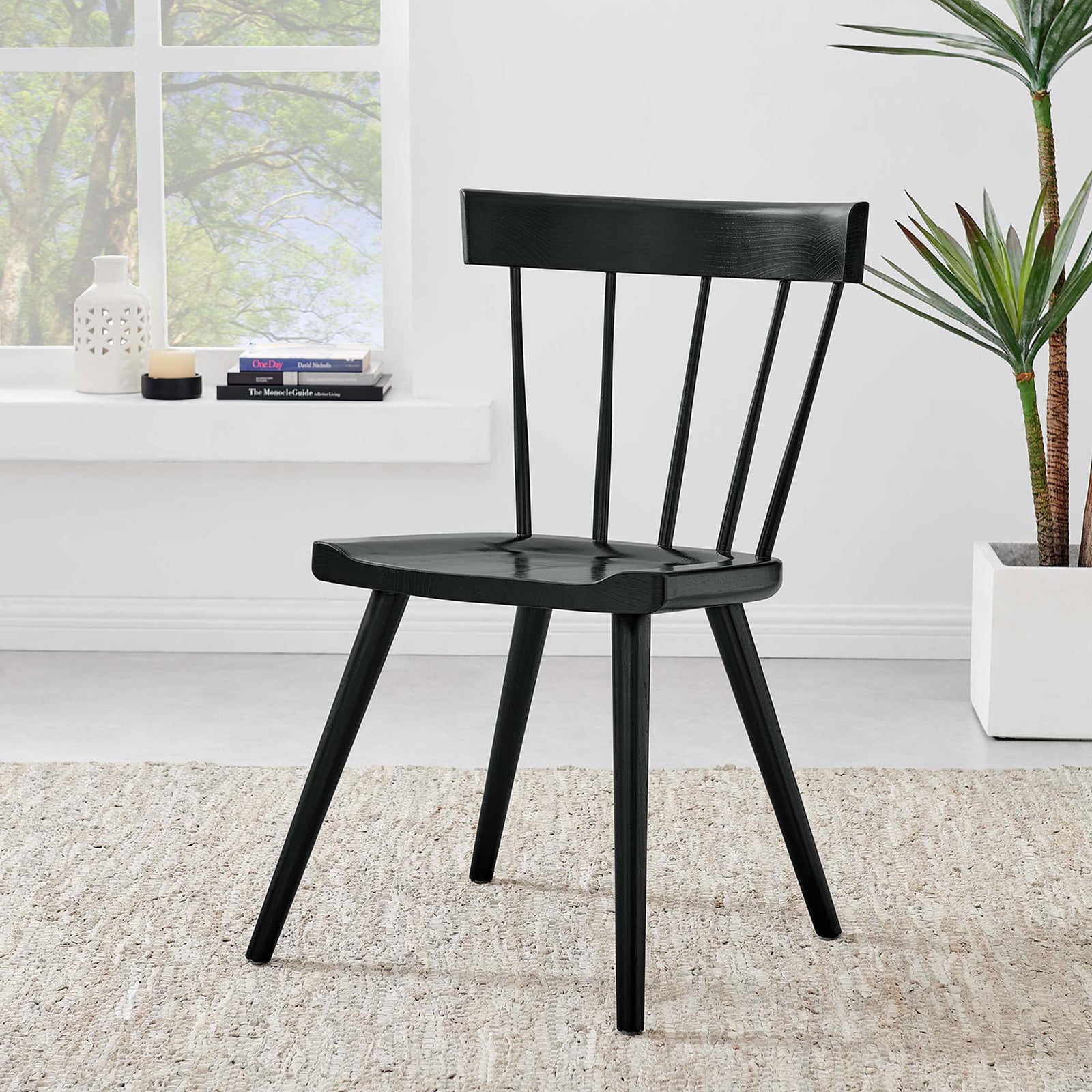 Black wood dining chair styled in a bright room with neutral rug, large window, and lush green plant. || EEI-4650-BLK || front_angle_room