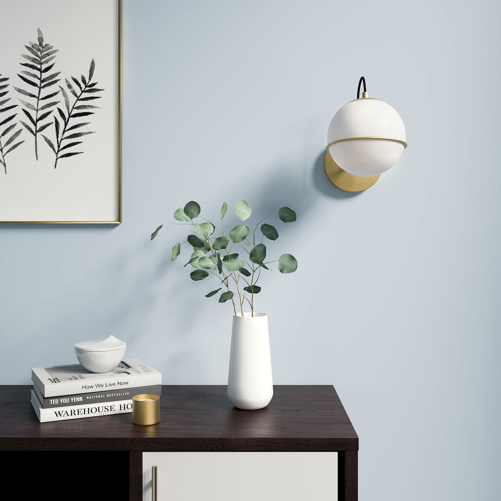 Opal globe wall sconce in satin brass styled above a console with greenery, books, and decor || EEI-5308-OPA-GLD || front_room
