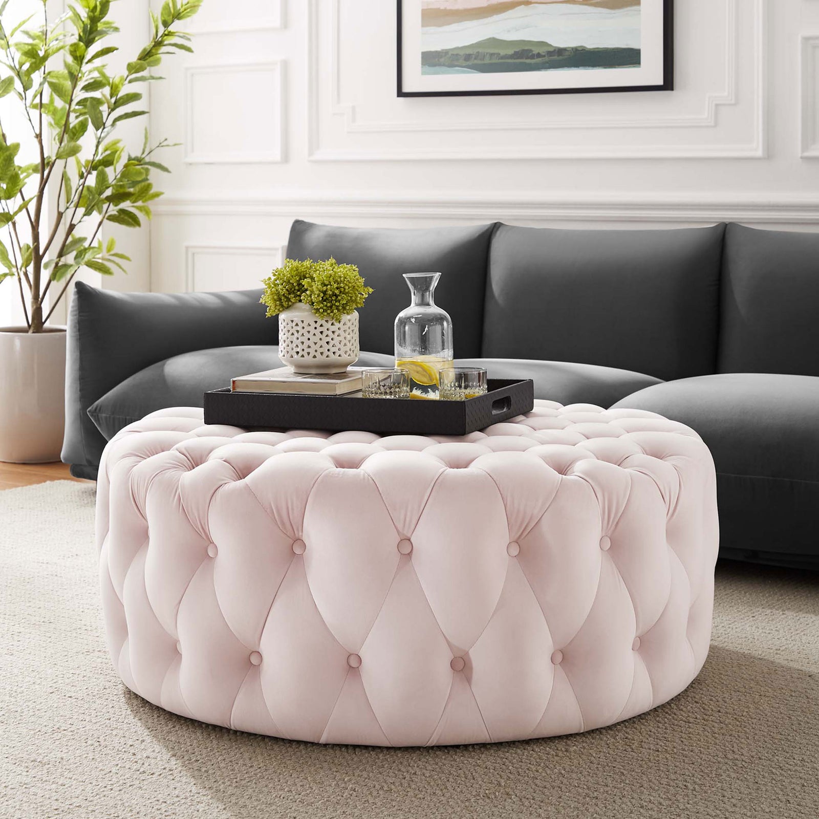Blush pink round tufted ottoman in a modern living room styled as a coffee table || EEI-5469-PNK || front_angle_room