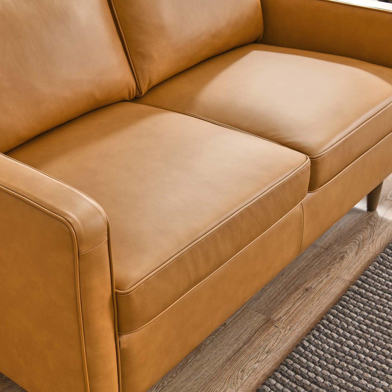 Tan leather loveseat seat cushions with smooth upholstery styled over warm wood floors and a textured rug. || EEI-5554-TAN || detail_room