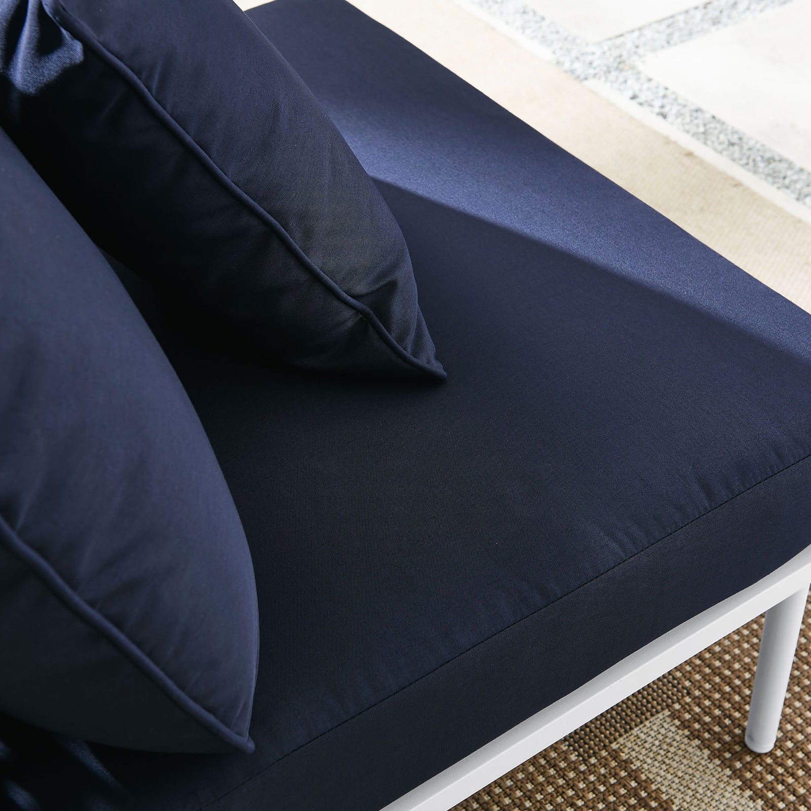 Plush navy cushions of the Stance armless chair resting on a patterned outdoor rug || EEI-5568-WHI-NAV || detail_room