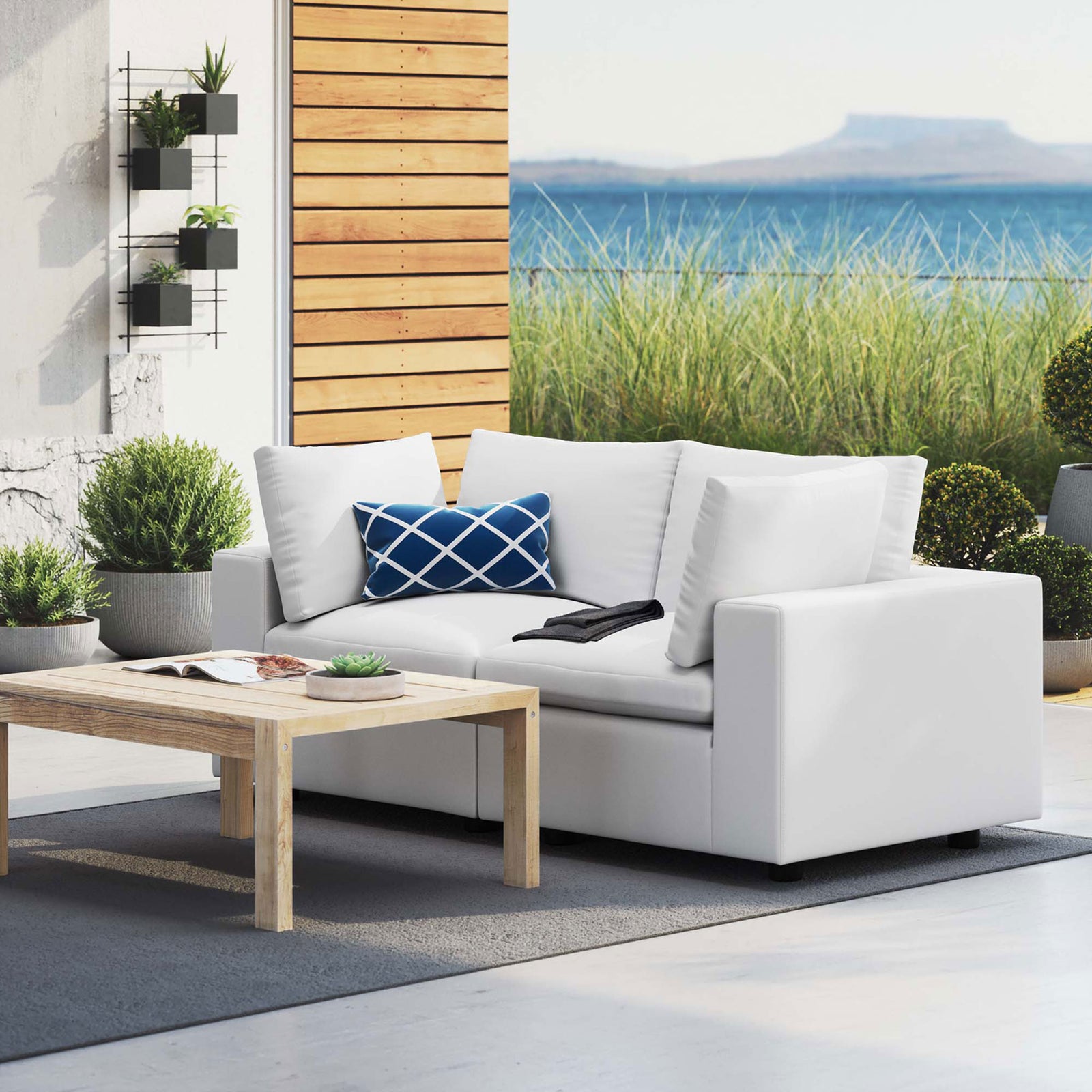 White outdoor loveseat on a contemporary patio with greenery and open sky beyond || EEI-5577-WHI || front_angle_room