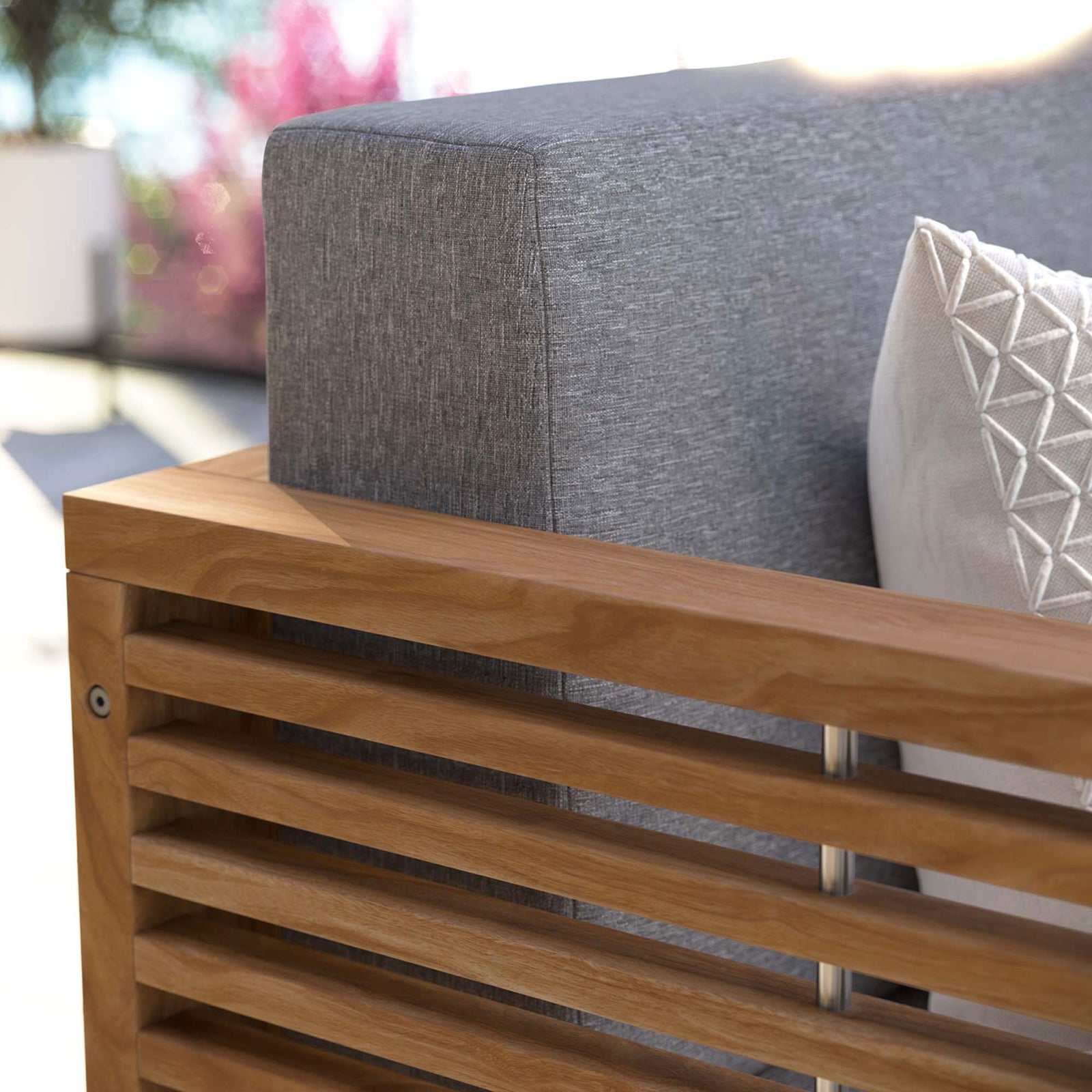 Outdoor close-up of the gray loveseat cushion and warm teak armrest styled with a patterned accent pillow. || EEI-5605-NAT-GRY || detail_room