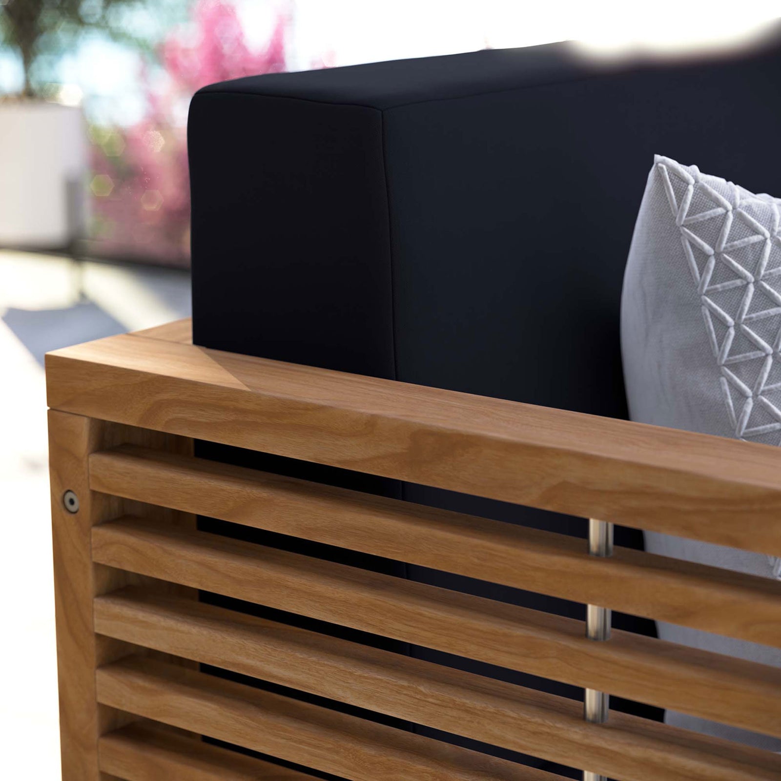 Outdoor close-up of the navy loveseat cushion and warm teak arm, accented with a textured decorative pillow. || EEI-5605-NAT-NAV || detail_room