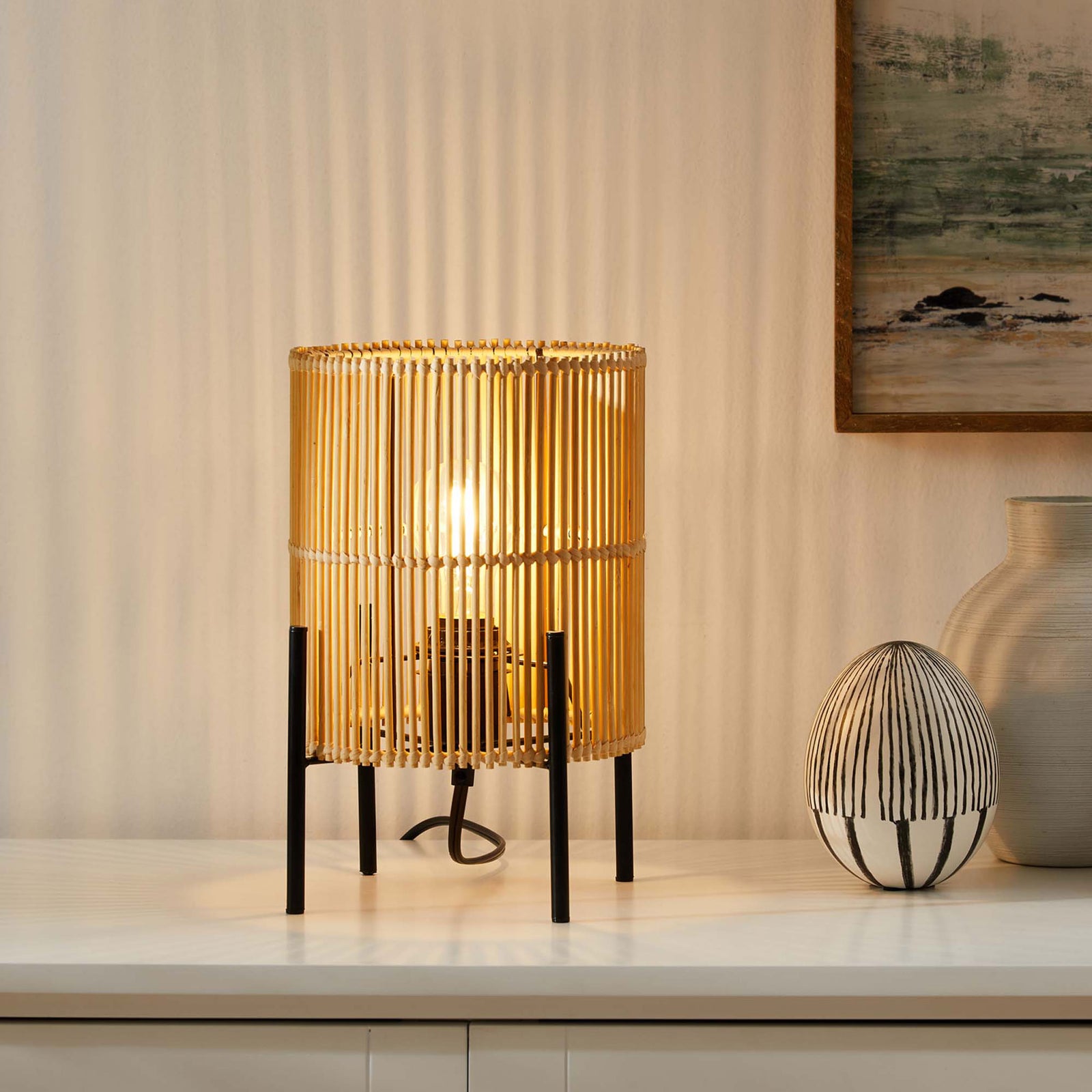 Casen bamboo table lamp glowing softly against the wall to create cozy layered ambient lighting || EEI-5610-NAT || front_angle_on_room