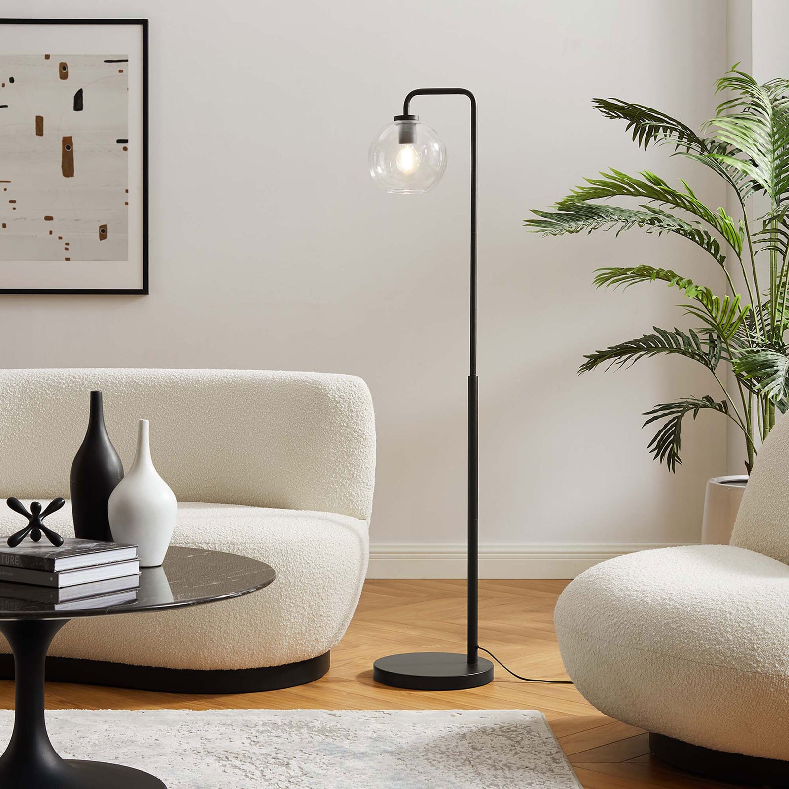 Silo black floor lamp with illuminated glass globe bringing warm light to a modern living room seating area || EEI-5616-BLK || front_angle_on_room