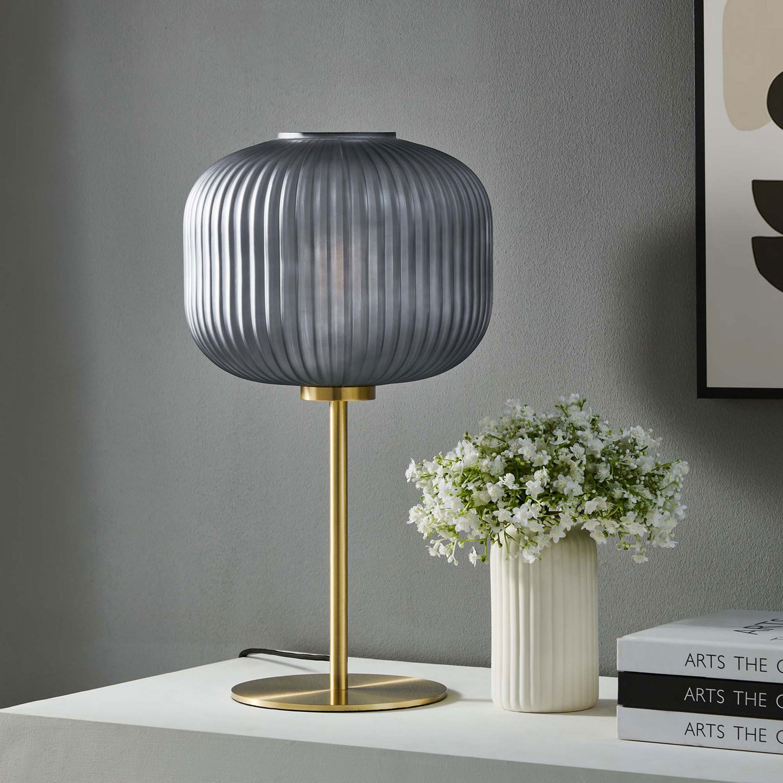 Smoked glass and satin brass table lamp styled on a console with white vase and art books || EEI-5622-BLK-SBR || front_room