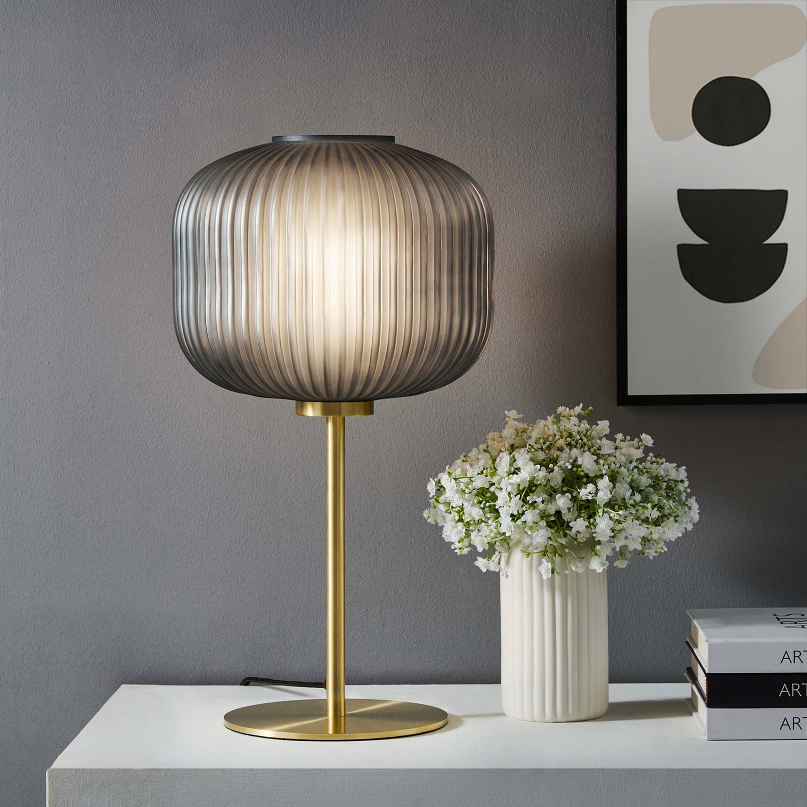 Smoked glass globe table lamp casting a warm ambient glow beside flowers and modern artwork || EEI-5622-BLK-SBR || front_on_room