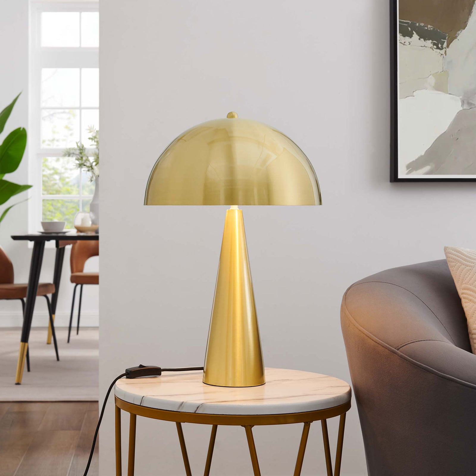 Selena satin brass table lamp glowing warmly on a marble side table in a modern living room || EEI-5624-SBR || front_on_room
