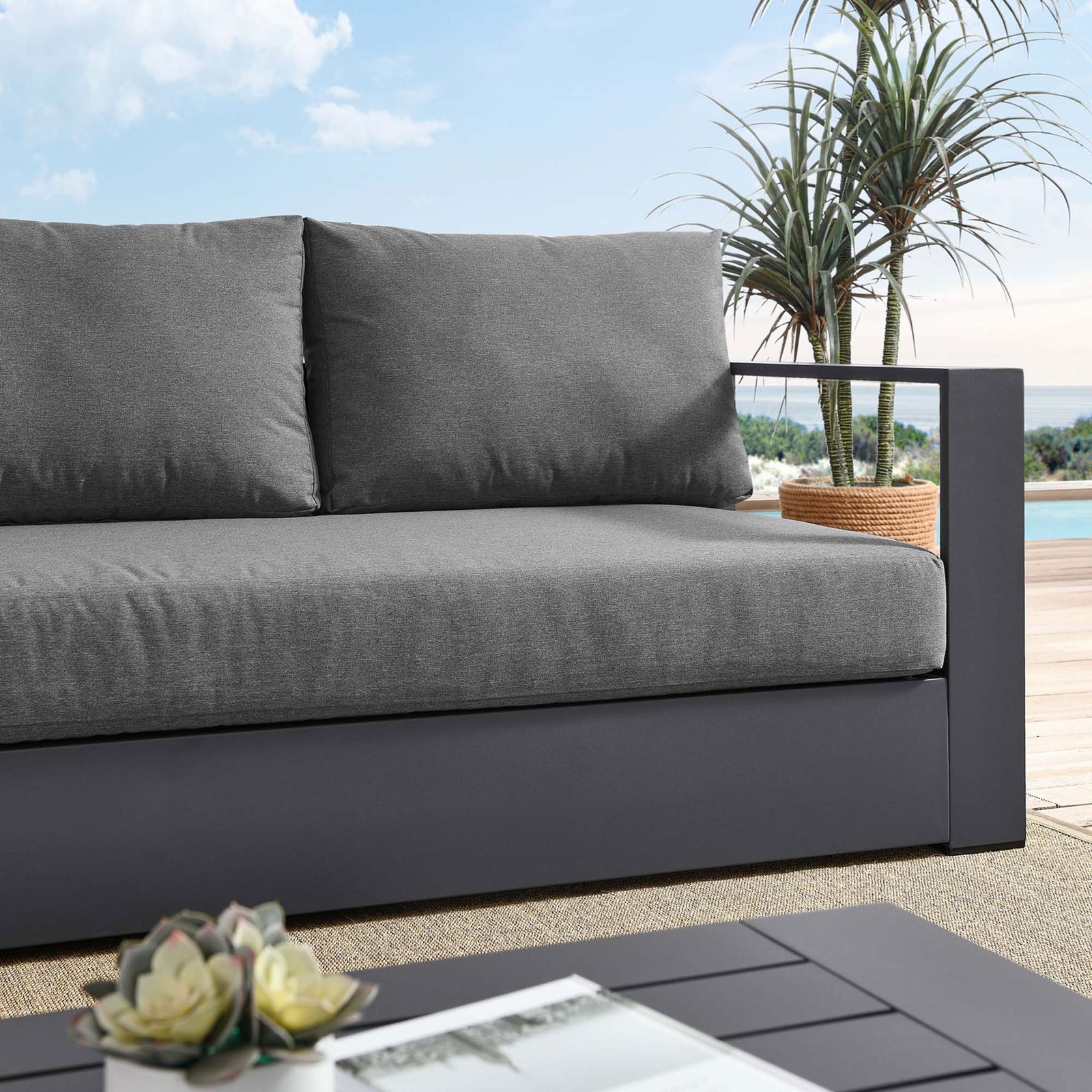 Close lifestyle view of the Tahoe sofa, pairing dark gray cushions with a charcoal frame on the patio. || EEI-5676-GRY-CHA || detail_room