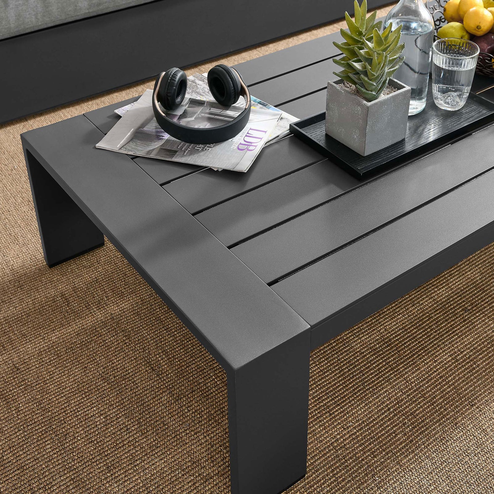 Gray aluminum coffee table styled with decor on a woven outdoor rug in a lounge setting || EEI-5677-GRY || detail_room