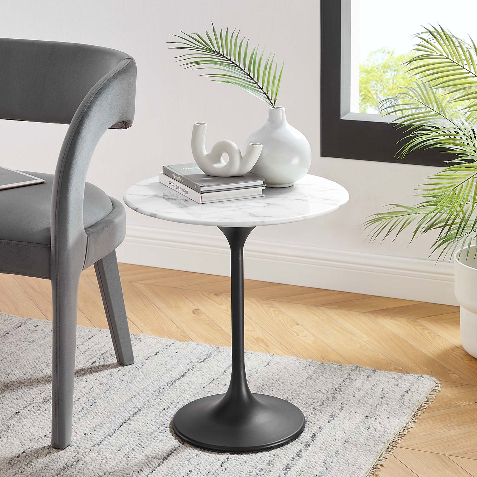 Round faux marble side table with black pedestal base styled next to a modern gray chair || EEI-5690-BLK-WHI || front_angle_room