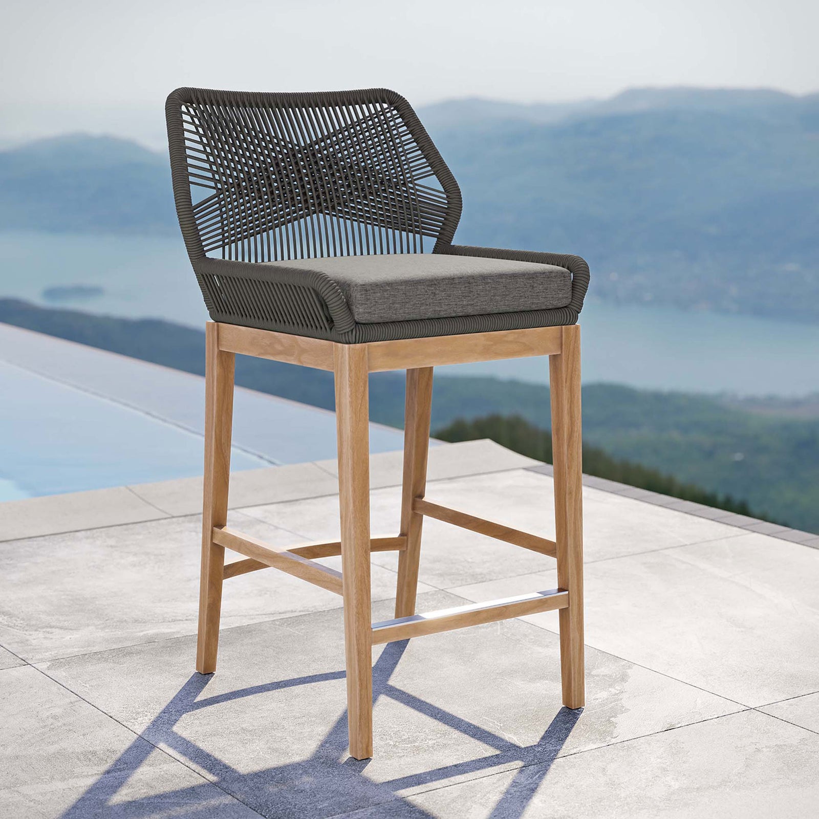 Gray graphite rope bar stool with cushioned seat and teak base styled on a contemporary poolside patio. || EEI-5746-GRY-GPH || front_angle_room